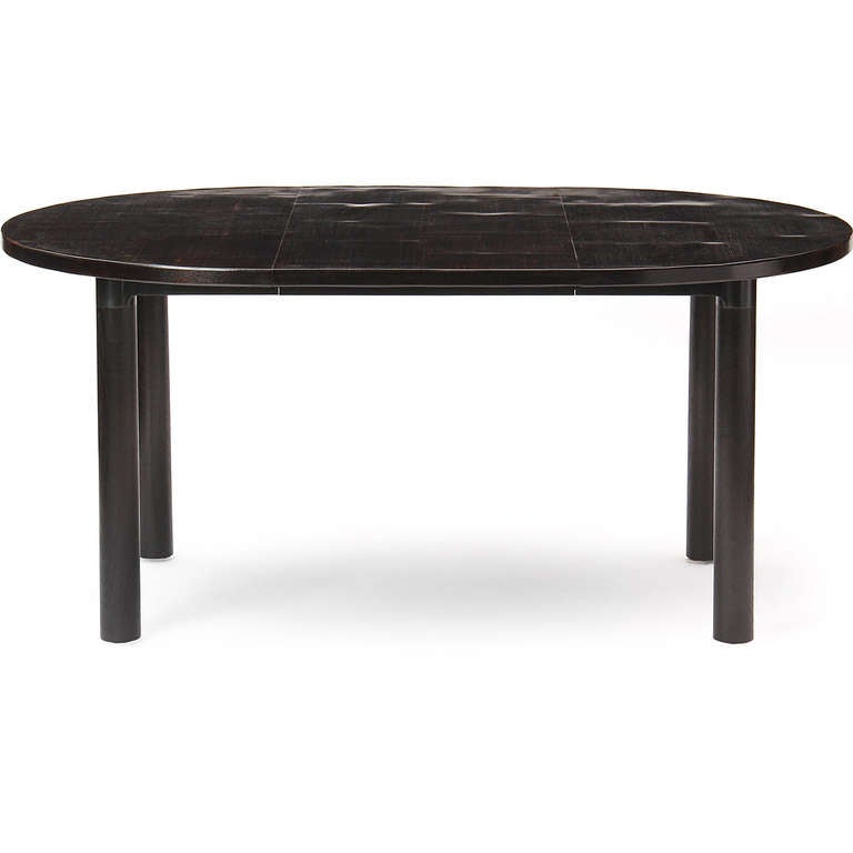 An impeccably-crafted round ebonized bamboo-top dining table with blackened steel legs that opens and expands to a wide oval with one 21