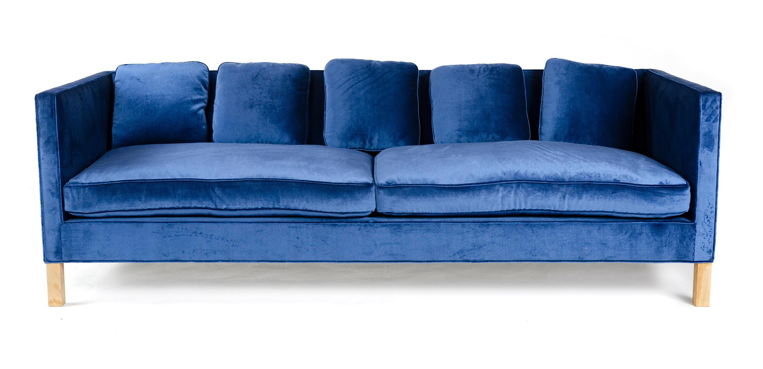 Un canapé smoking minimal avec un cadre en bois massif et des ressorts noués à la main, avec des coussins remplis de duvet et des dossiers recouverts de velours de coton bleu.

  