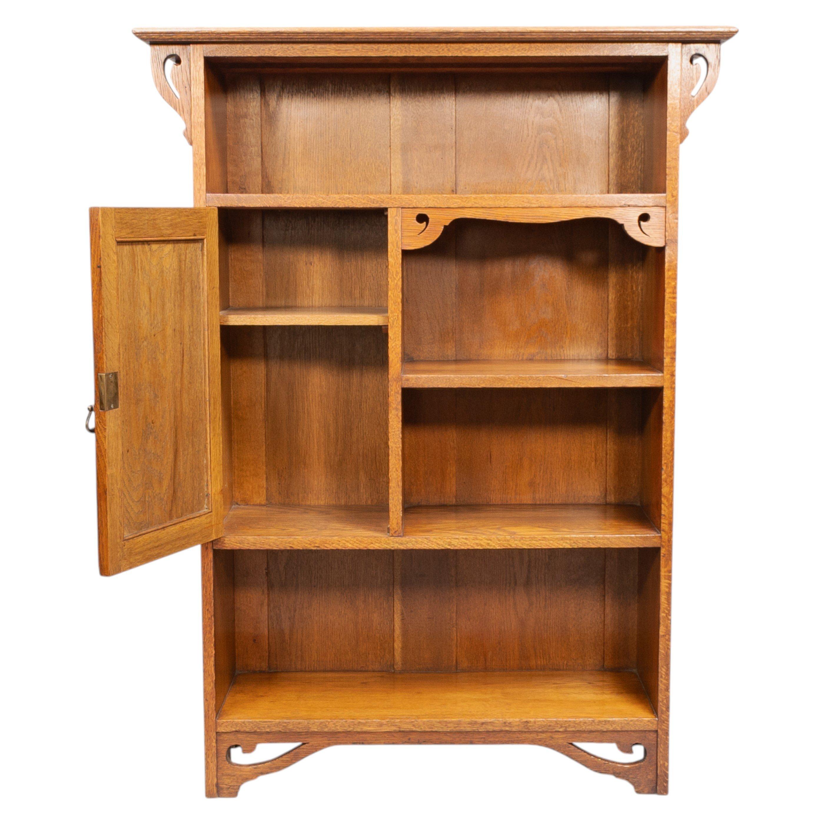 Wylie and Lochhead of Glasgow, in the style of. An Arts and Crafts oak open bookcase with a cupboard to the left. The cupboard door is inlaid with fine floral decoration, while the upright supports are enriched with decorative fretwork curls.