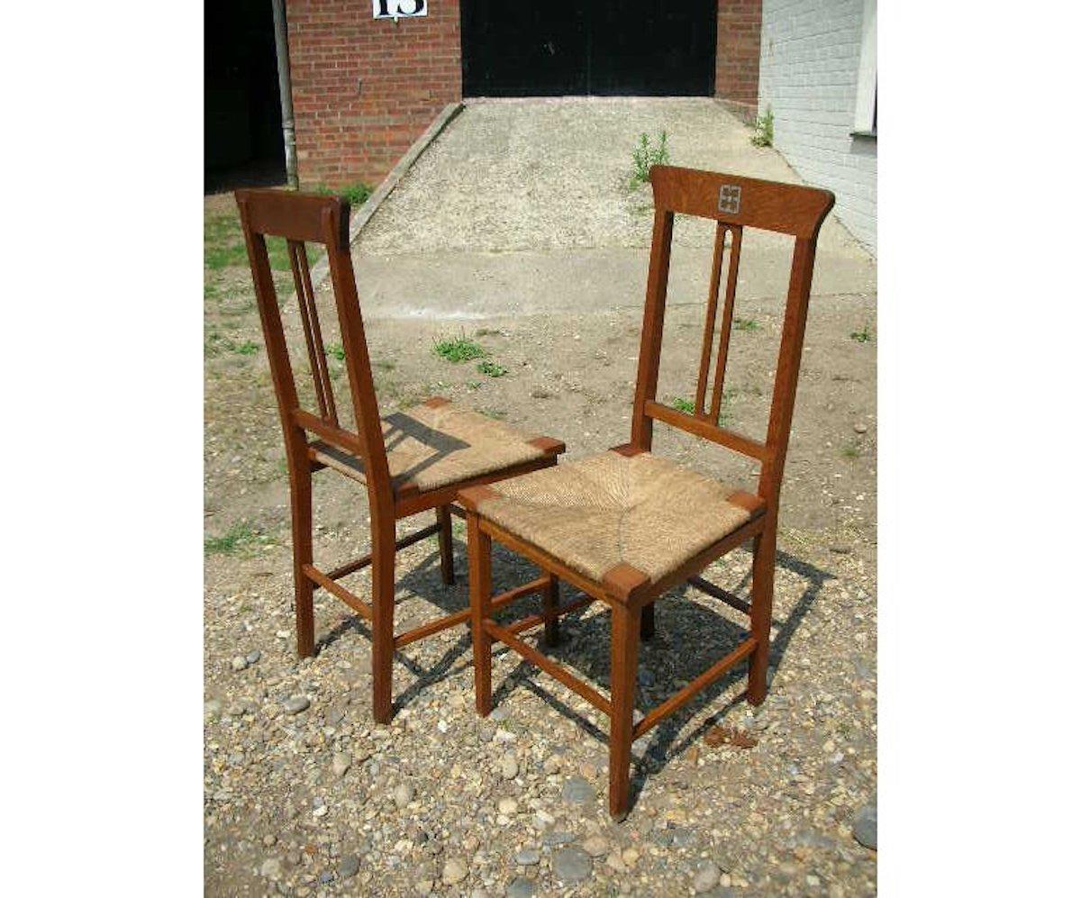 Wylie & Lochhead. A pair of Glasgow School oak Arts & Crafts bedroom chairs, with inlaid pewter florets to the top, retaining their original rush seats which although faded are in good condition, with square tapering legs united by four