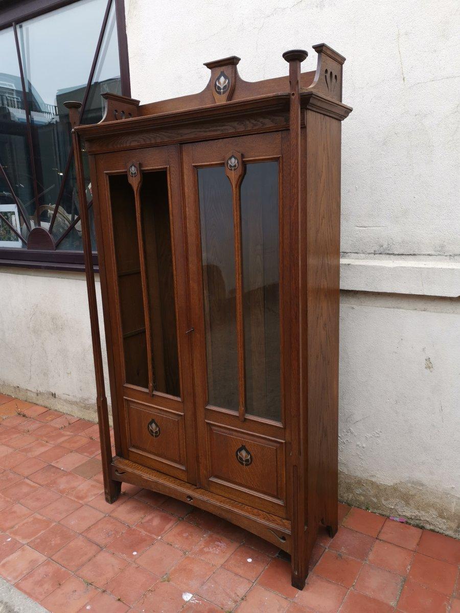 Wylie and Lochhead Attributed. An Arts & Crafts oak and glazed two door bookcase in the style of C F A Voysey with circular caps for candles to the front uprights which are set slightly forward of the doors. An open top shelf with a full width plate