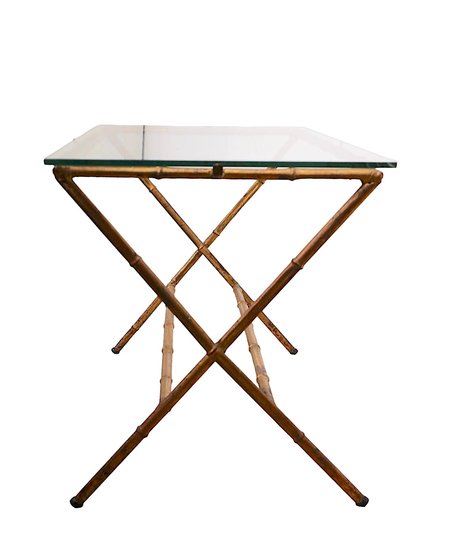 Table d'appoint ou de chevet chic, élégante et sophistiquée, avec une base en faux bambou en forme de X, en finition dorée d'origine, et un plateau en verre d'origine. La table est en très bon état, propre et prête à l'emploi, ne présentant qu'une
