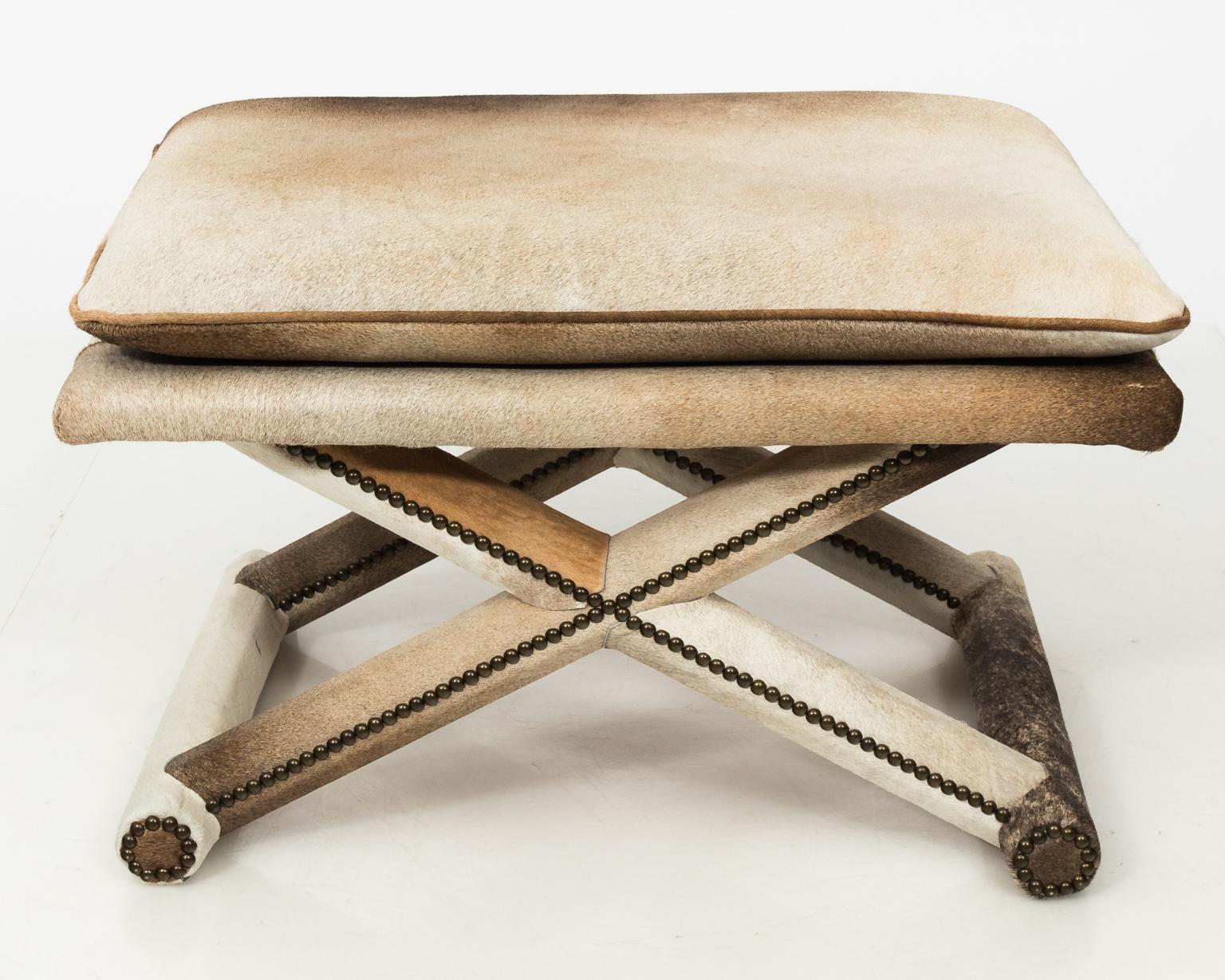 X form bench or stool completely upholstered in cowhide, with attached seat cushion and decorative nail heads.
 