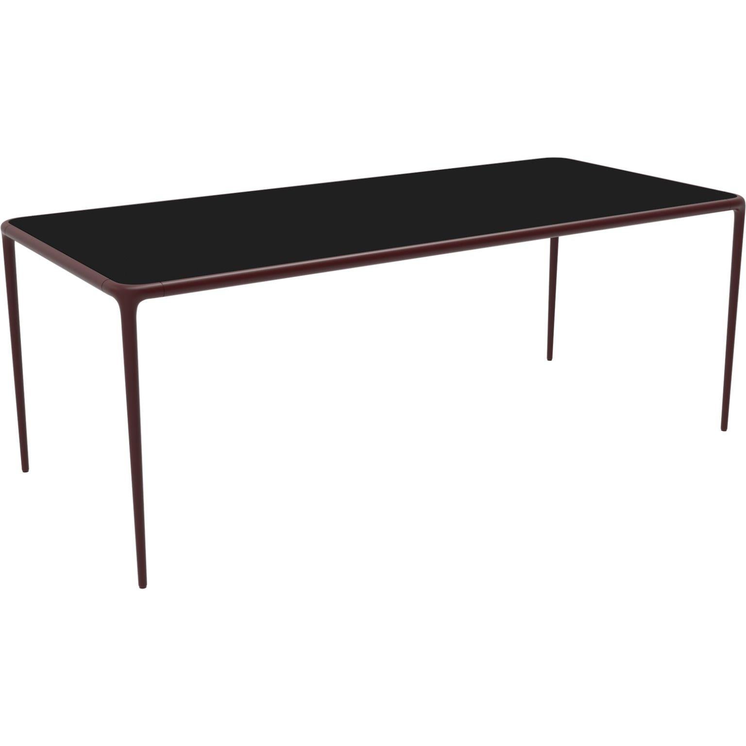 Xaloc burgundy glass top 200 table by MOWEE
Dimensions: D200 x W90 x H74 cm
Material: Aluminium, tinted tempered glass top.
Also available in different aluminum colors and finishes (HPL Black Edge or Neolith). 

Xaloc synthesizes the lines of