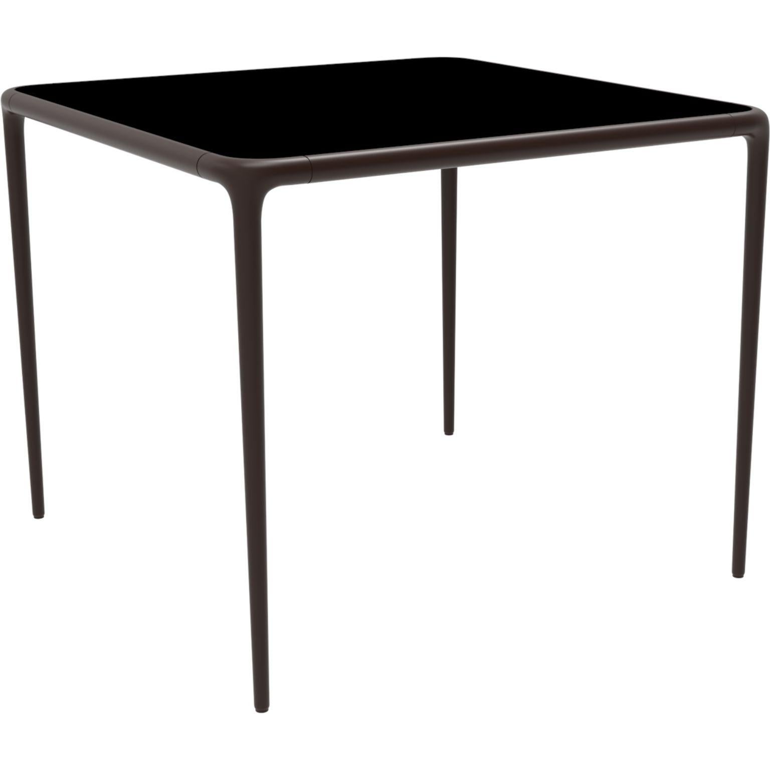 Xaloc chocolate glass top table 90 by MOWEE
Dimensions: D90 x W90 x H74 cm
Material: Aluminum, tinted tempered glass top.
Also available in different aluminum colors and finishes (HPL Black Edge or Neolith). 

 Xaloc synthesizes the lines of
