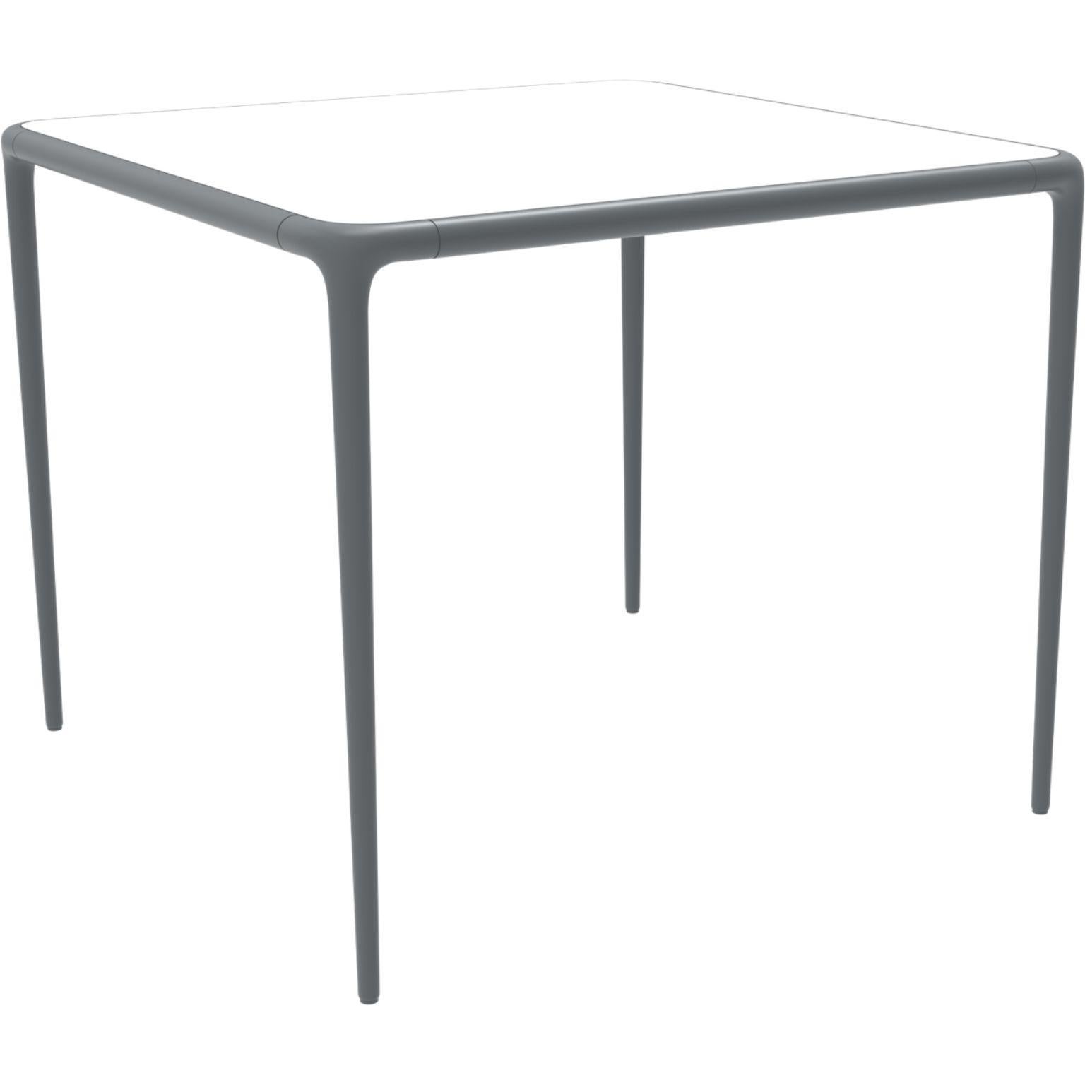Xaloc grey glass top table 90 by Mowee.
Dimensions: D90 x W90 x H74 cm.
Material: Aluminum, tinted tempered glass top.
Also available in different aluminum colors and finishes (HPL Black Edge or Neolith). 

 Xaloc synthesizes the lines of