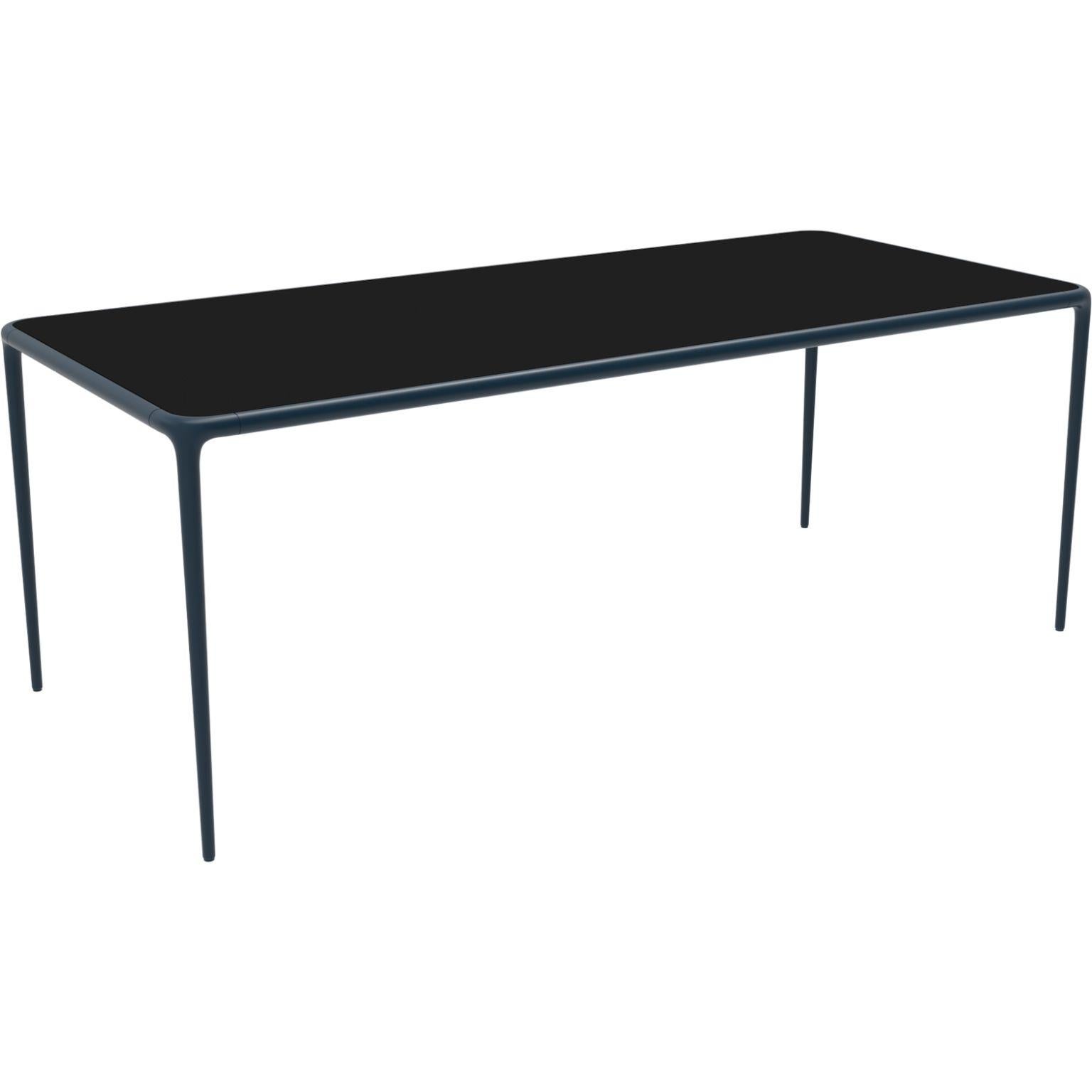 Xaloc navy glass top 200 table by MOWEE
Dimensions: D200 x W90 x H74 cm
Material: Aluminium, tinted tempered glass top.
Also available in different aluminum colors and finishes (HPL Black Edge or Neolith). 

Xaloc synthesizes the lines of