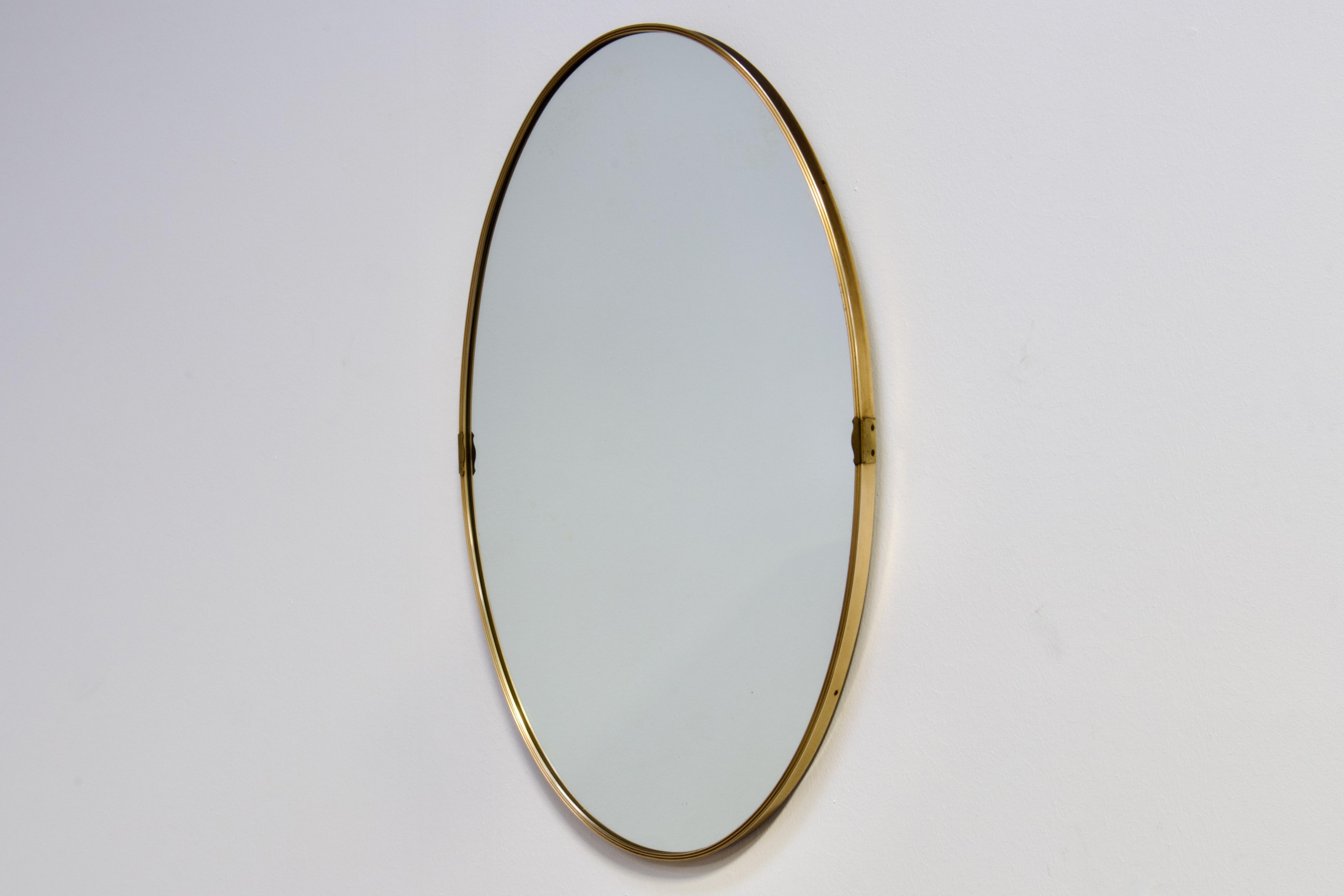 Large Gio Ponti era Mid-Century Modern wall mirror in patinated brass. Made in Italy in 1950s.

The shape of the mirror is a very elegant oval, symmetrical both horizontally and vertically. The face of the brass frame is ridged to give a subtle but