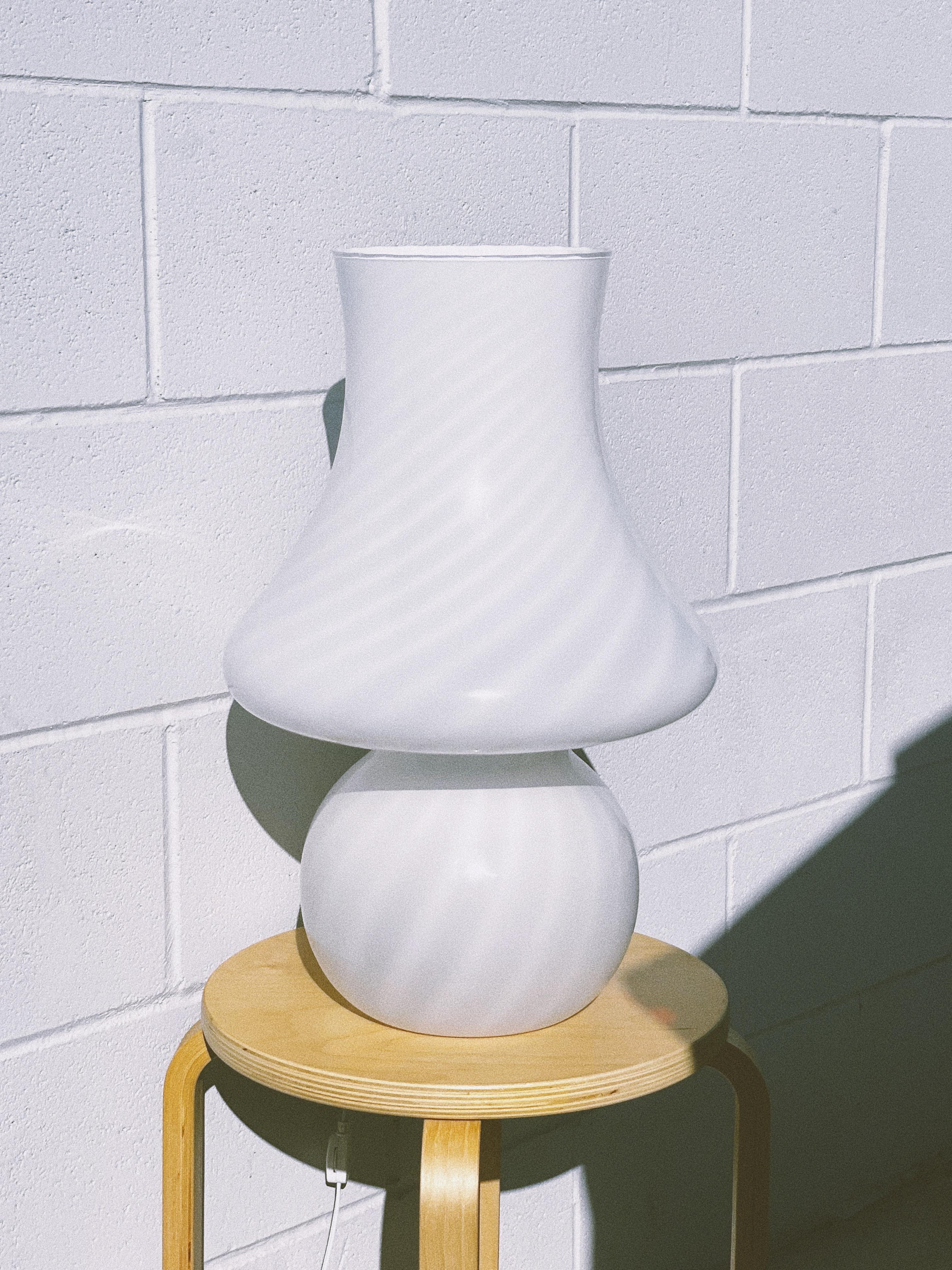 The XL 1960s Murano glass lamp by Vetro Artistico offers a classic, timeless appeal in its milky white, swirled design. The lamp emits a warm and diffused glow when it is turned on.