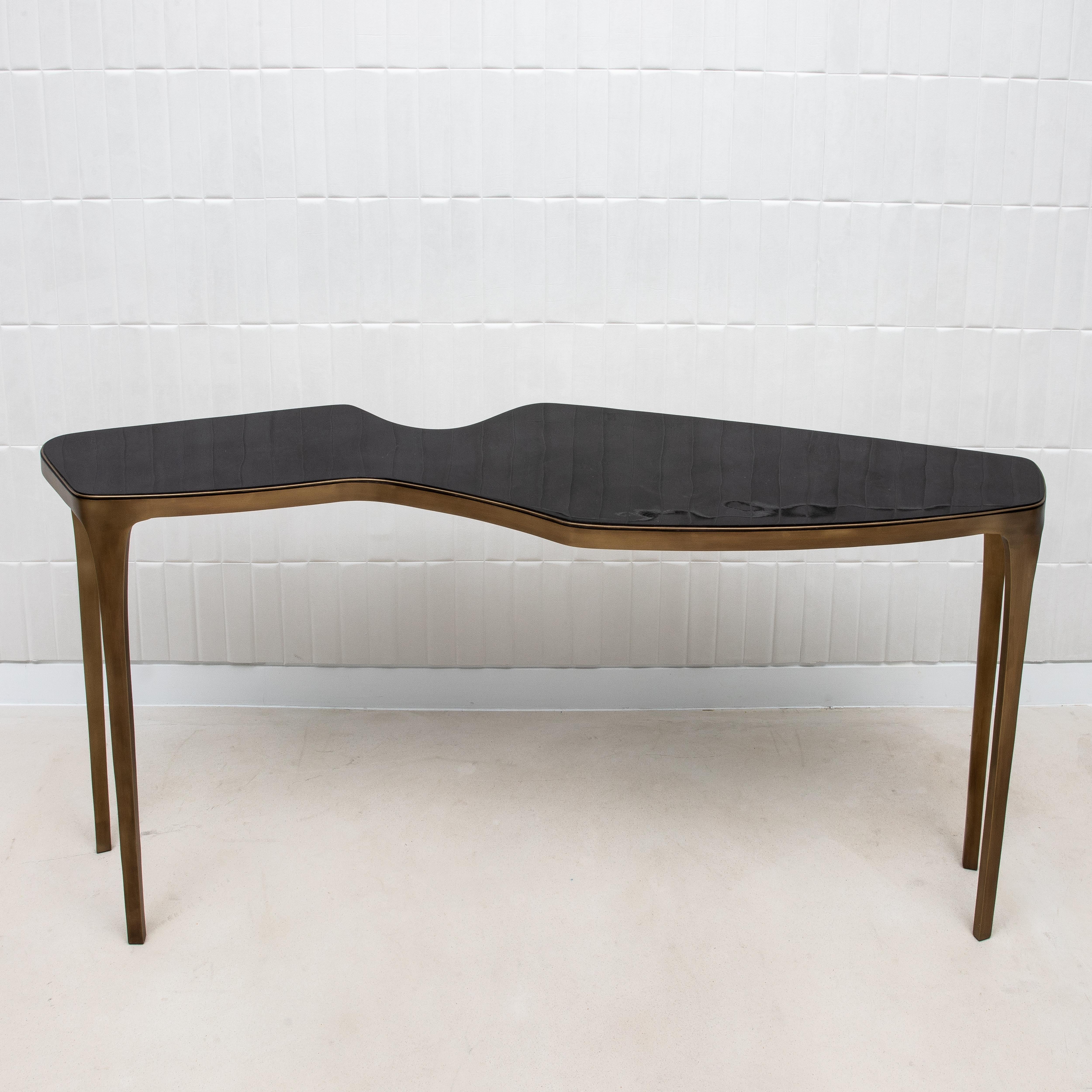 The Cosmos Console by R&Y Augousti showcases a distinctive, asymmetrical shape that flows like a ribbon, creating a dynamic and eye-catching silhouette. This undulating design, coupled with the reflective pen shell surface, evokes the organic forms
