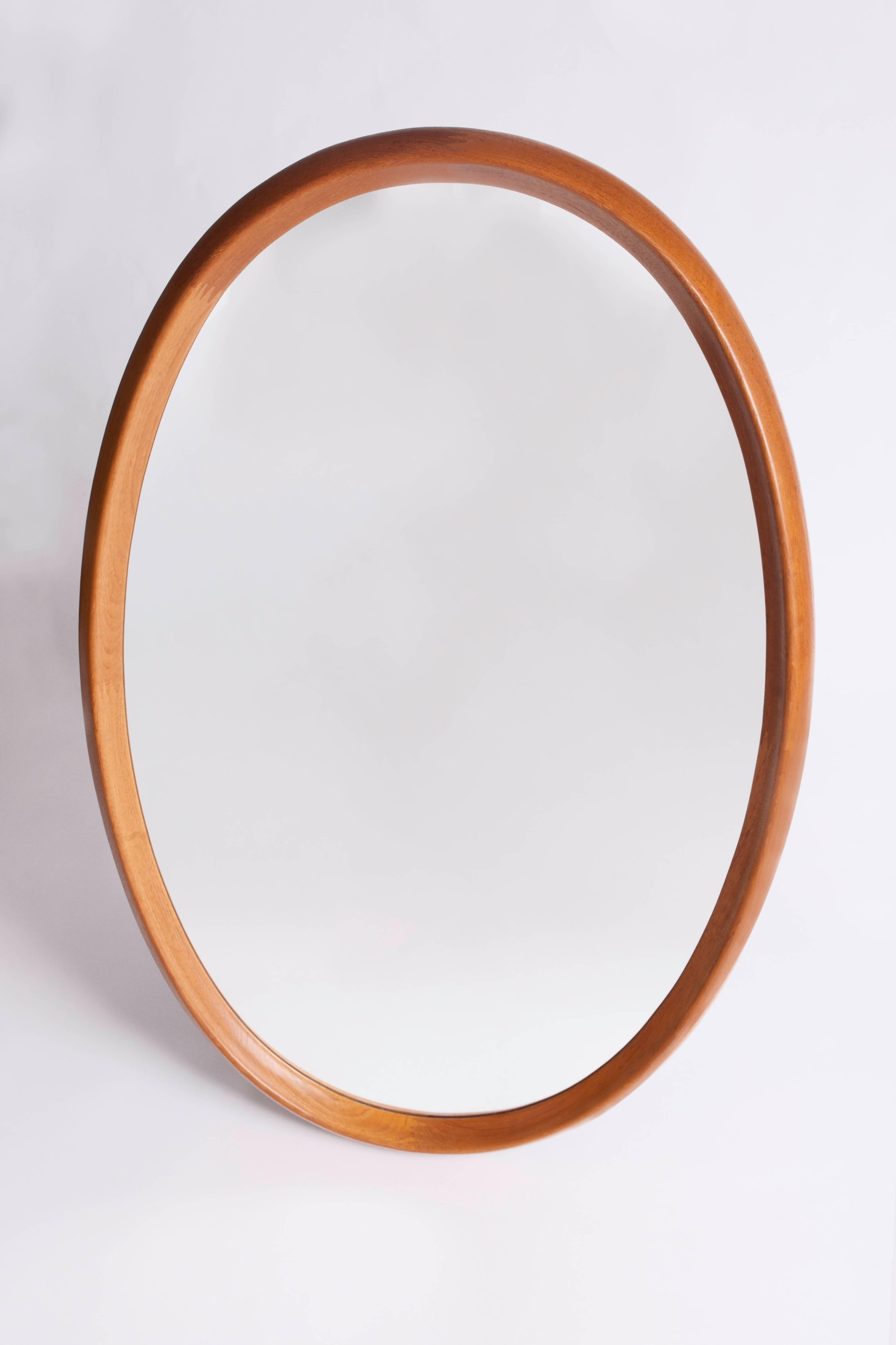 A monumental, finely crafted Scandinavian Modern oval mirror with a geometric zipper motif by Pedersen & Hansen. In sculptural two-inch thick teak, with a deep and curved bevel and beautiful two-tone interlocking dovetail joinery. Denmark, 1960's.