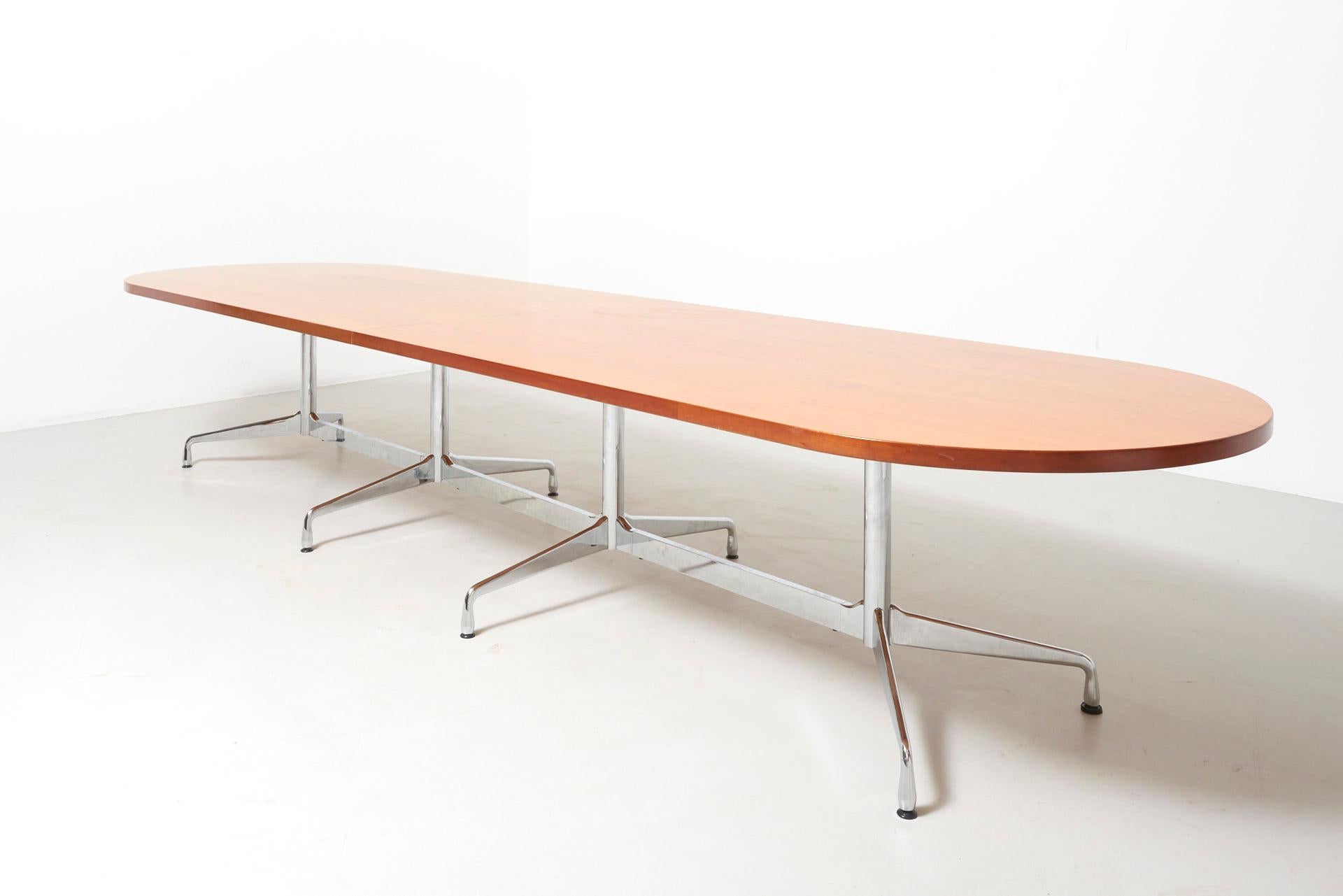 A large conference table in cherry veneer on a chrome base. Design by Charles and Ray Eames in the 1950s. This version of the segmented base table has 4 legs offering space for at least 16 people. The top is made of 2 parts which are fastened with