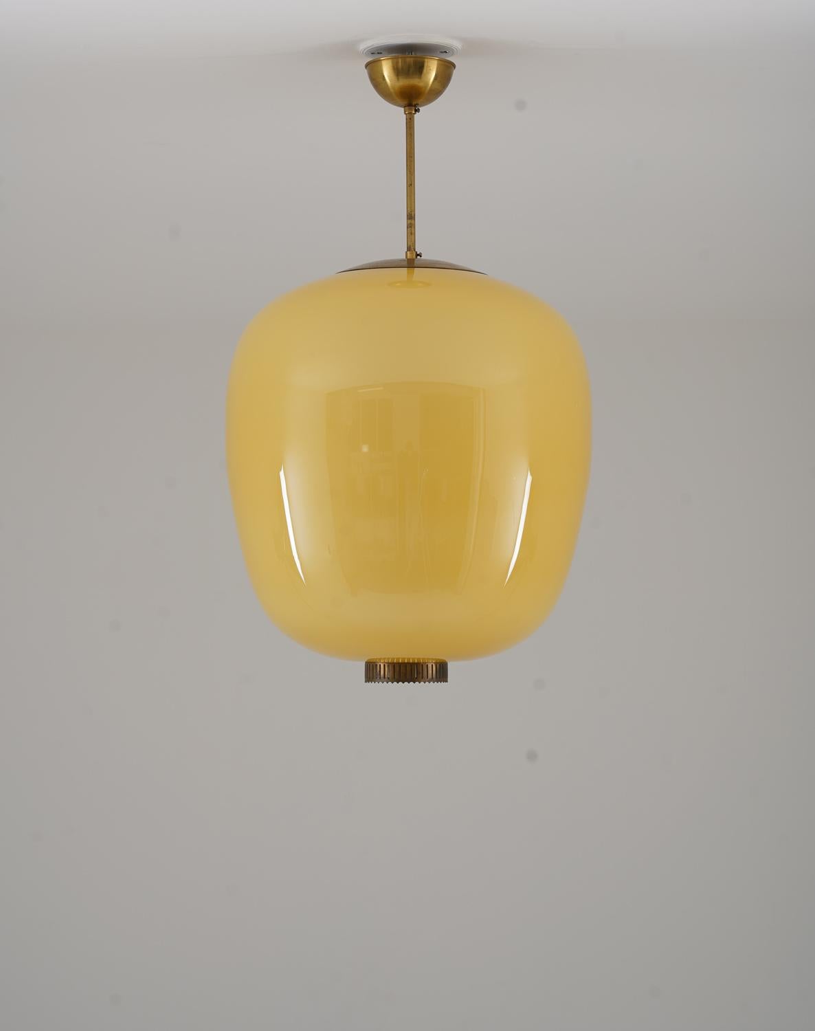 Pair of rare Swedish Modern pendants in brass and glass, manufactured in Sweden during the 1940s. The globes are crafted using an advanced three-layer glass technique, ensuring optimal light diffusion and a rich, warm glow. The amber-hued glass