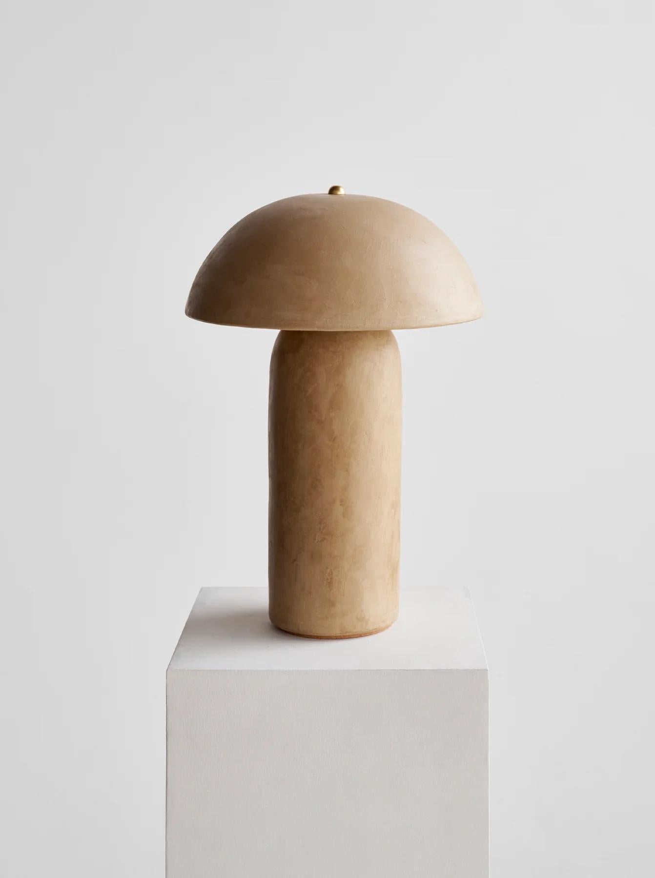 Die Tera Lamp - Lime Plaster von Ceramicah besteht aus einem radgedrehten Keramikschirm und einem Keramikfuß. Nachdem die Keramikstücke den Ofen durchlaufen haben, wird der Kalkputz in zwei Schichten von Hand aufgetragen, glatt geschliffen und mit