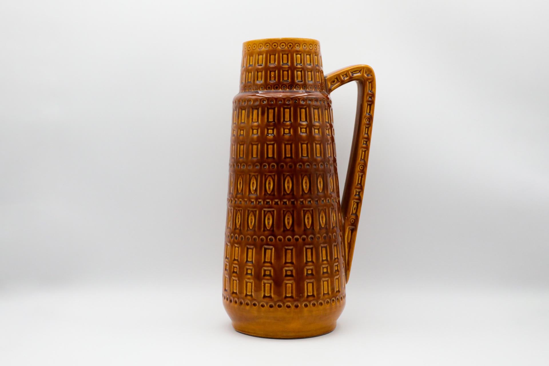 Très grande cruche en céramique de l'Allemagne de l'Ouest avec poignée. Vase tambour rond et effilé, à glaçure brun doré et à motifs sculptés de carrés et de cercles. En état d'origine avec une usure conforme à l'âge et à l'utilisation. Marqué
