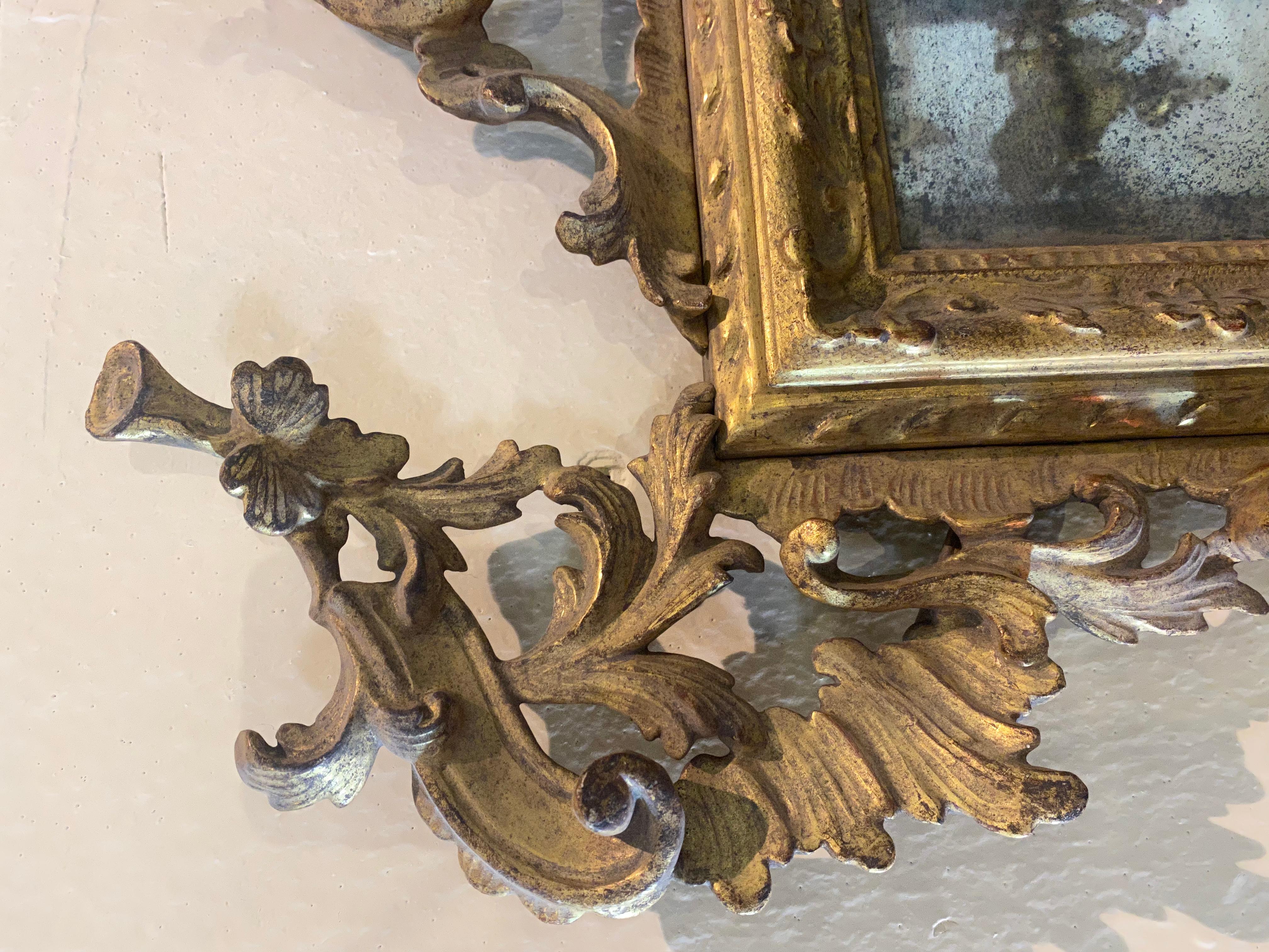 Vollständig geschnitzt und vergoldet. Geschmückt mit einer reichhaltigen, mit Rocaille-Laubsägearbeiten versehenen Kappe, in deren Mitte sich ein kleiner Rahmen mit Wellenprofil befindet, der auch mit einem alten Originalspiegel ausgestattet ist.