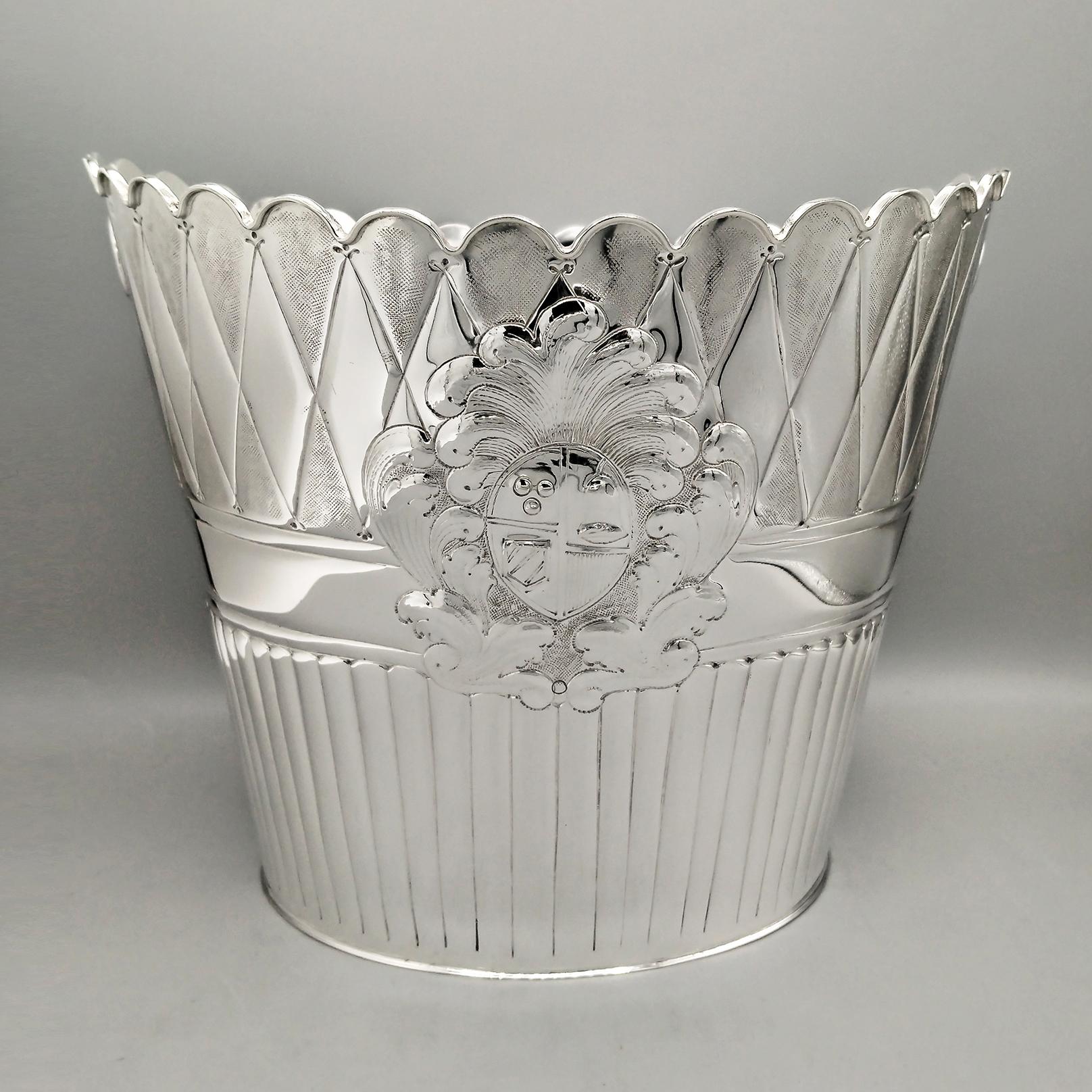 Cubo ovalado de plata de ley para champán.
La forma del cuerpo es ovalada que se ensancha en la parte superior terminando con un festón redondo en forma de regalo.
El cuerpo se ha repujado y grabado con distintos motivos, con rayas en la parte