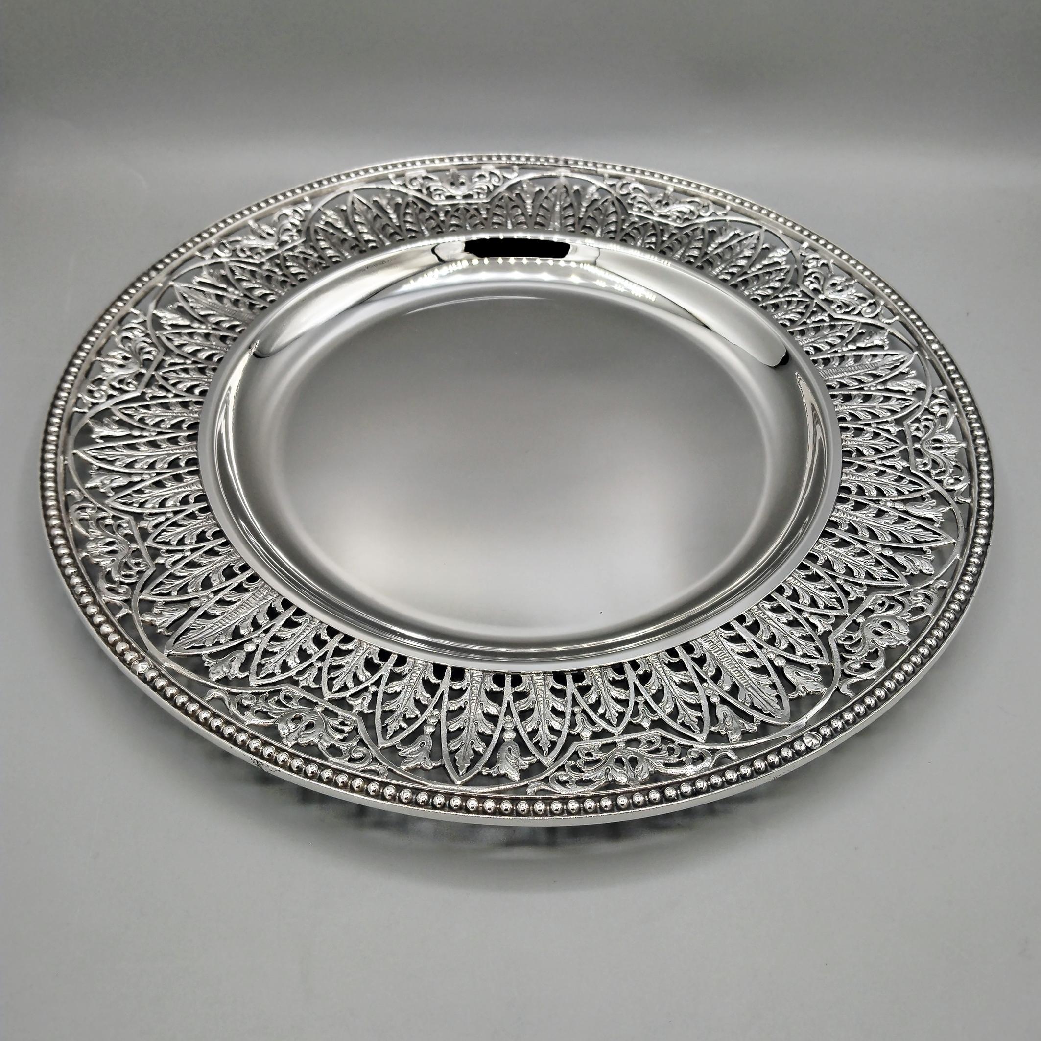 Plaque ronde en argent massif 800, faite à la main.
L'assiette, lisse au centre, présente un bord créé par la technique de la fonte, puis fini au ciseau, représentant des feuilles et des volutes.
L'assiette est complétée par une bordure perlée