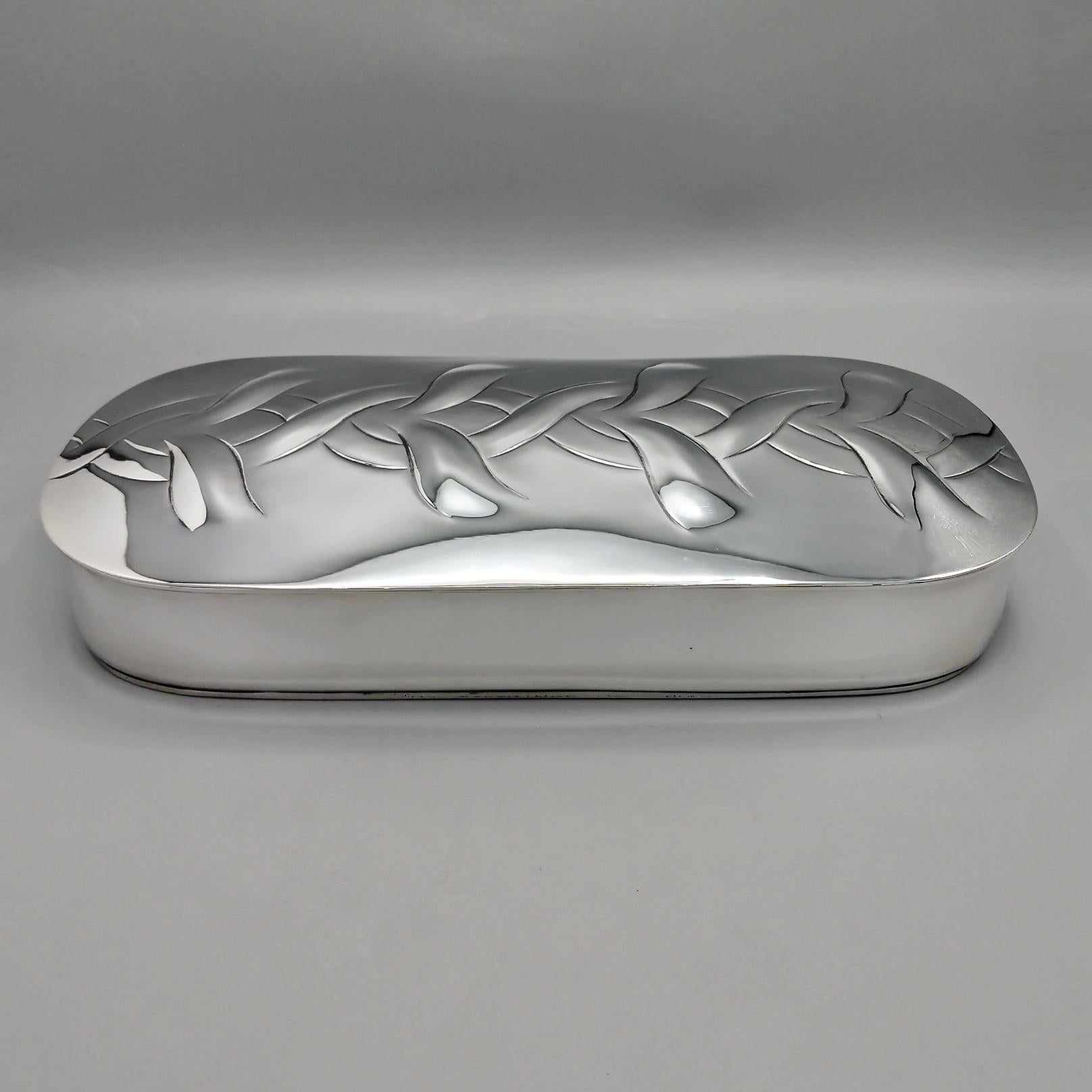 Caja decorativa de mesa oblonga en plata de ley 925.
El fondo de la caja se moldeó a mano a partir de una lámina de plata de ley, se martilló y se remató con un borde plano.
La tapa, abisagrada y ligeramente redondeada, se repujó y luego cinceló con