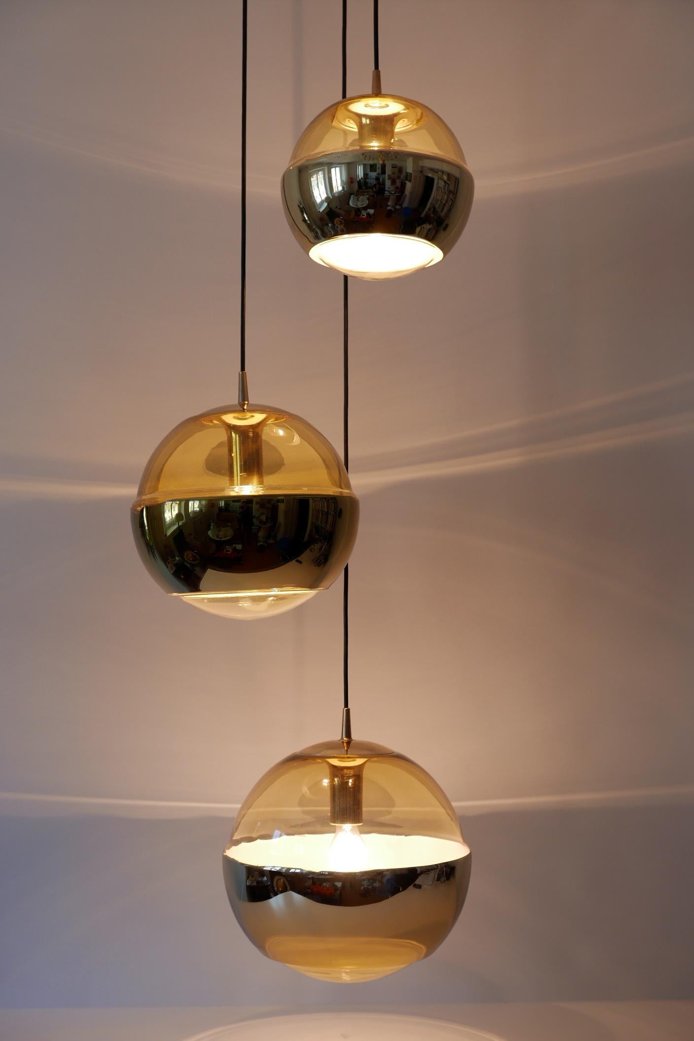 Elegant and large Mid-Century Modern chandelier or cascading pendant lamp: Three amber colored glass shades with gold stripes. Manufactured by Peill & Putzler, Düren, Germany, 1970s. 

Executed in amber colored glass and brass. It needs 3 x E27