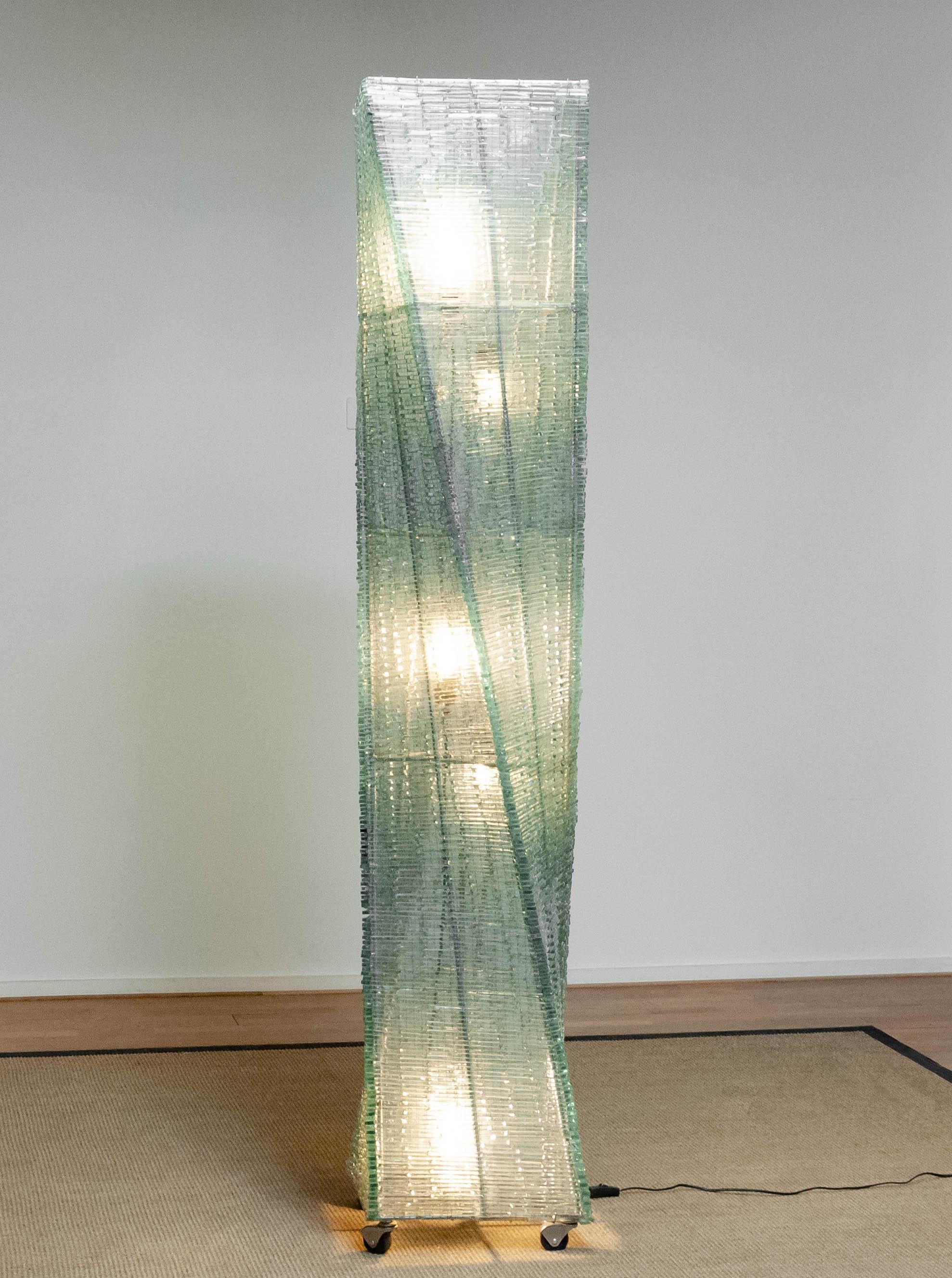 This impressive floor lamp is a true light sculpture, made from vertically stacked layers of ribbed safety glass, shaped into a striking twisted silhouette. The transparent panels create a dynamic optical effect that shifts as you move around the