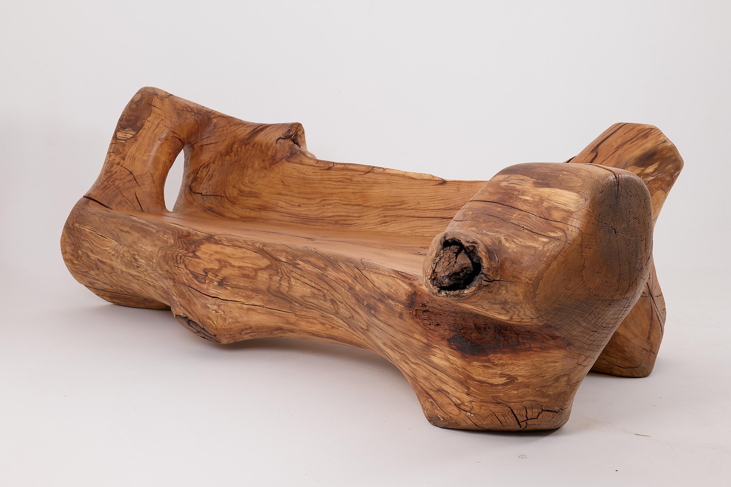 Una forma natural preservada y refinada, este banco esculpido está tallado íntegramente en una sola pieza maciza de madera maciza. Su forma orgánica se hace eco de los contornos brutos del árbol original, ofreciendo a la vez un asiento funcional y