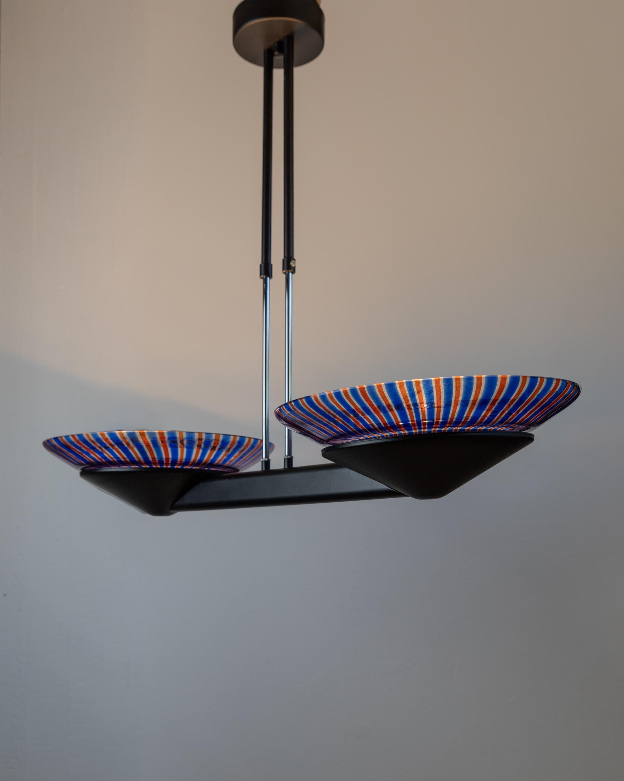 Questo lampadario vintage XXL in vetro di Murano, risalente agli anni '80, è un pezzo forte in pieno stile Memphis. Caratterizzato da una struttura minimale in metallo nero e da due grandi paralumi in vetro di Murano a righe blu, rosse e
