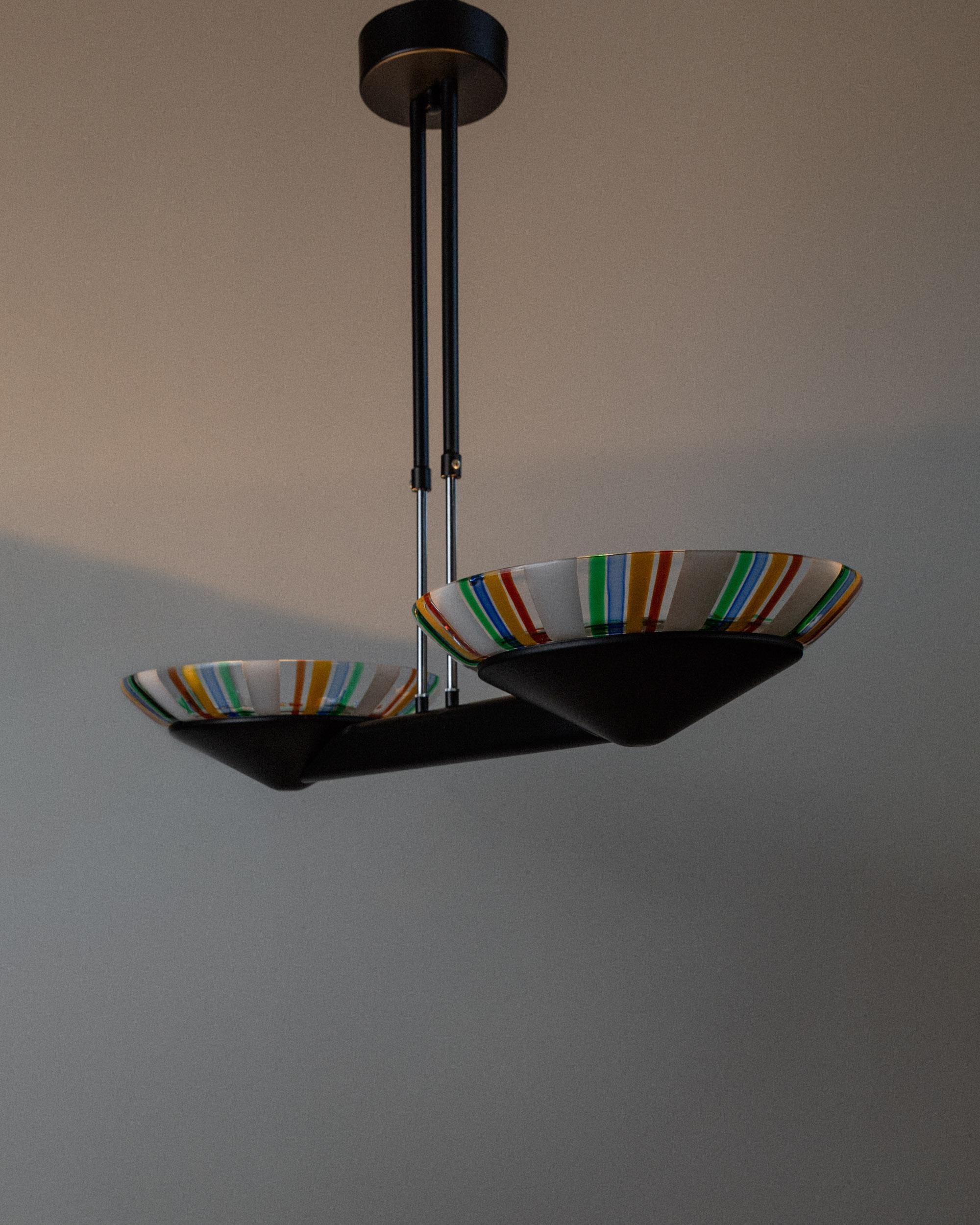 Questo lampadario vintage XXL in vetro di Murano, risalente agli anni '80, è un pezzo forte in pieno stile Memphis. Caratterizzato da una struttura minimale in metallo nero e da due grandi paralumi in vetro di Murano a righe colorate, aggiunge un