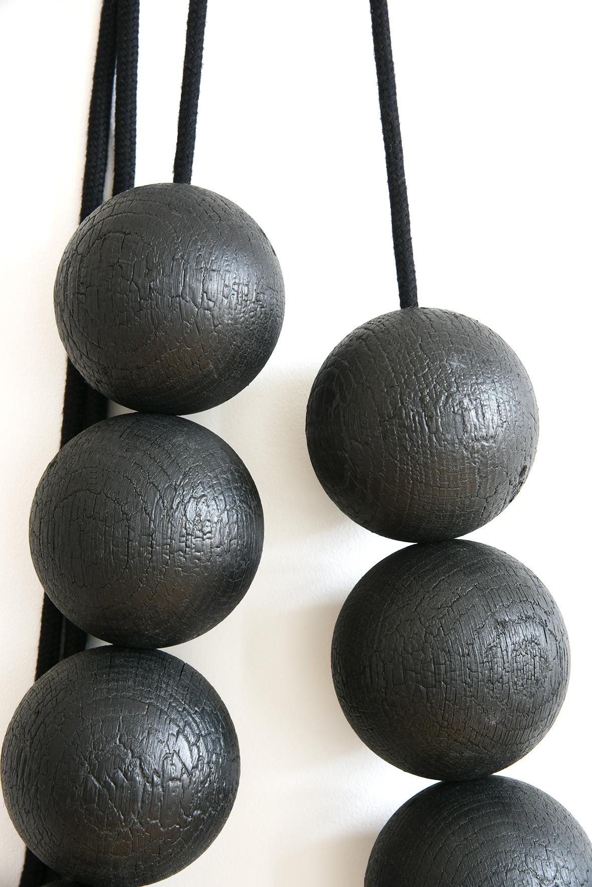 Collana da parete con sfere di legno XXL, finitura in legno bruciato secondo la cosiddetta tecnica Shou-sugi-ban, di origine giapponese. Con un trattamento superficiale naturale per stabilizzare la carbonizzazione, non lascia segni neri al tatto.
