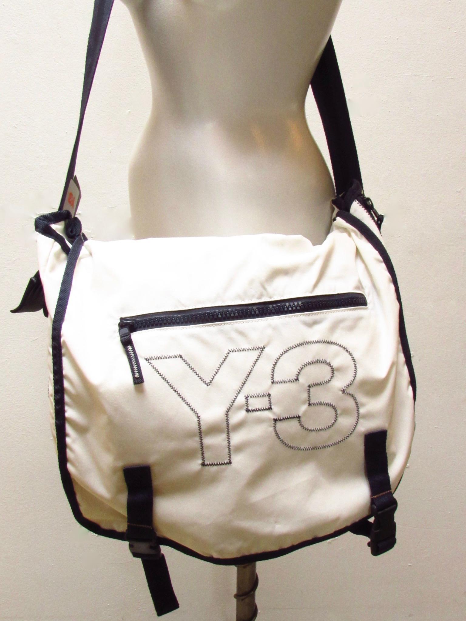 Le sac de messager en nylon blanc et bleu marine de Y-3 Yohji Yamamoto est léger et durable. Il est doté d'un rabat extérieur, avec une poche zippée, qui se fixe avec des clips. À l'intérieur, il y a plusieurs fentes pour organiser le contenu. Des