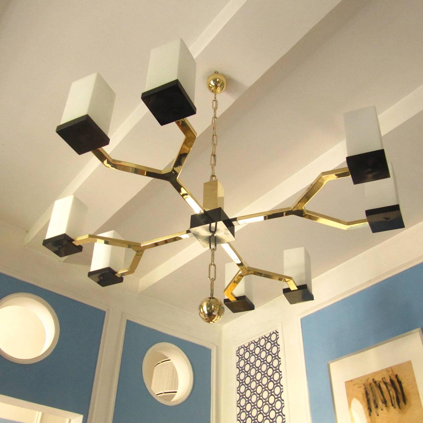 This eight-light chandelier features a hand-polished brass structure with accents of black-finished brass. The chain that supports the piece is in brass and each shade is in white glass. The lights are E 14.
