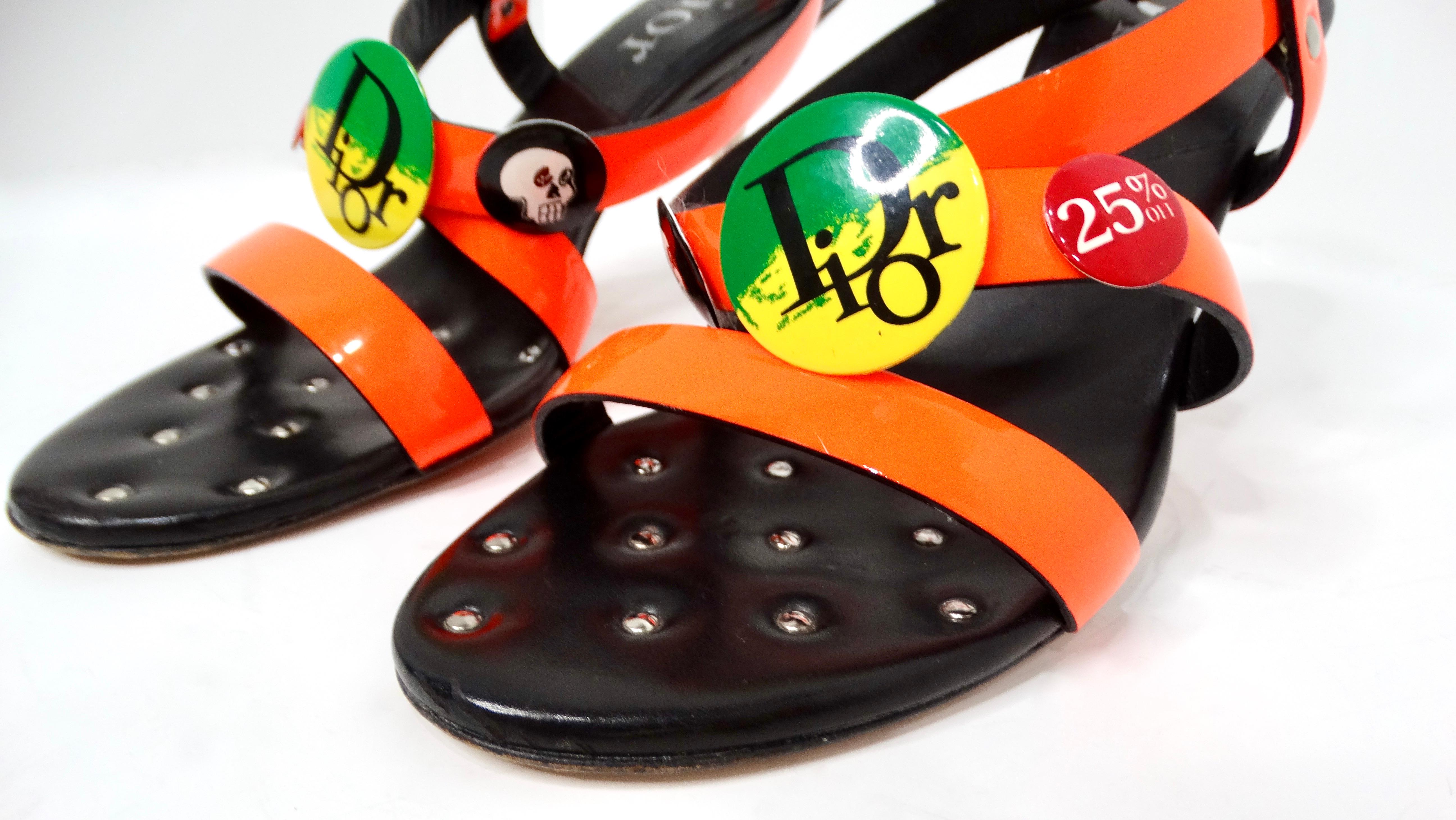 Entra nell'audace regno della moda dell'anno 2000 con le scarpe John Galliano x Christian Dior Neon Rasta Badge Patent Leather Sandal Heels. Realizzati in pelle verniciata arancione vibrante, questi tacchi sono un pezzo forte che racchiude