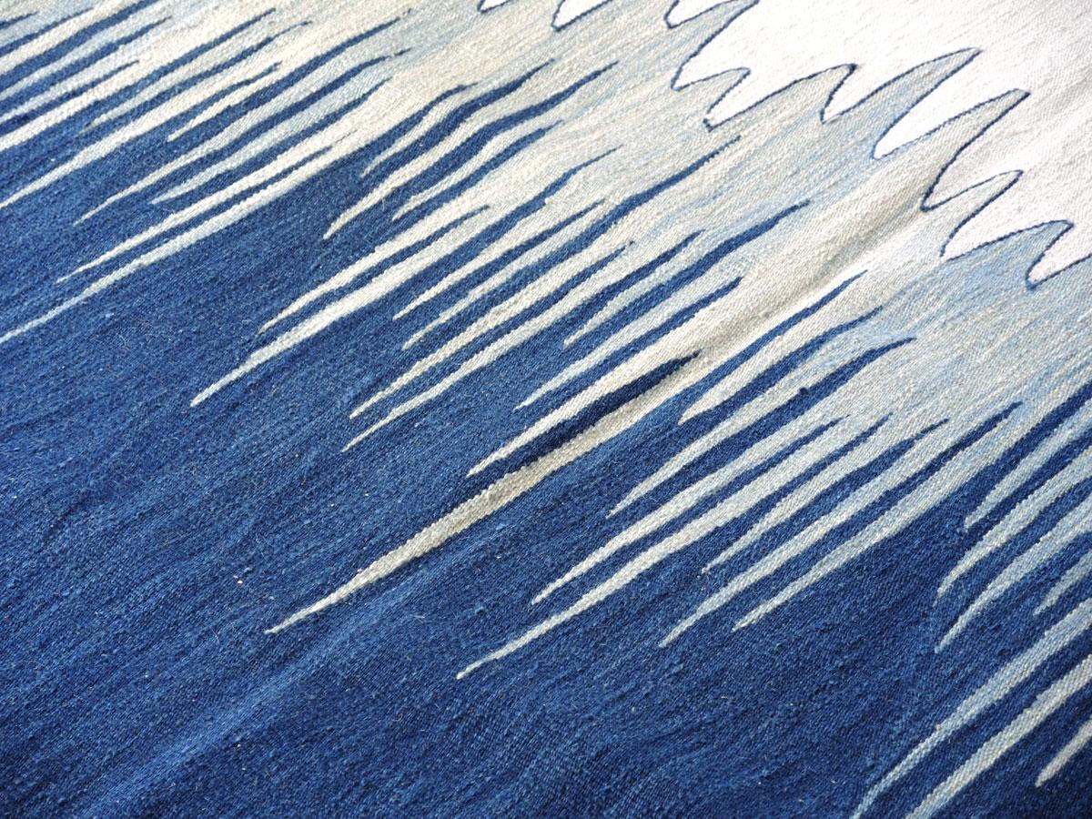 Der Kelimteppich Yakamoz No 4 gehört zu einer Serie von Kelims, die von der Poesie der Lichtreflexe auf der Meeresoberfläche inspiriert sind. Die abstrakten Muster, die an wechselnde Farbübergänge durch reflektiertes Licht erinnern, werden von