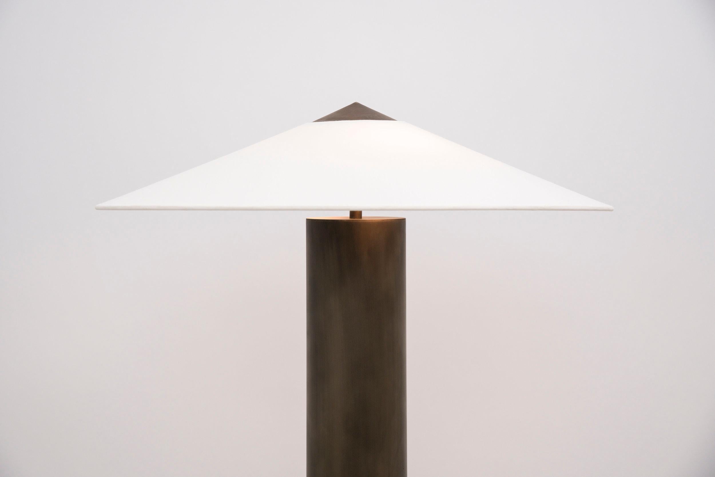 This symmetrical table lamp is comprised of an aged-brass base and a custom linen shade, which is supported by a hand-turned aged-brass CAP that continues the shade’s profile. The shade shape is inspired by a mountain and the aged-brass base