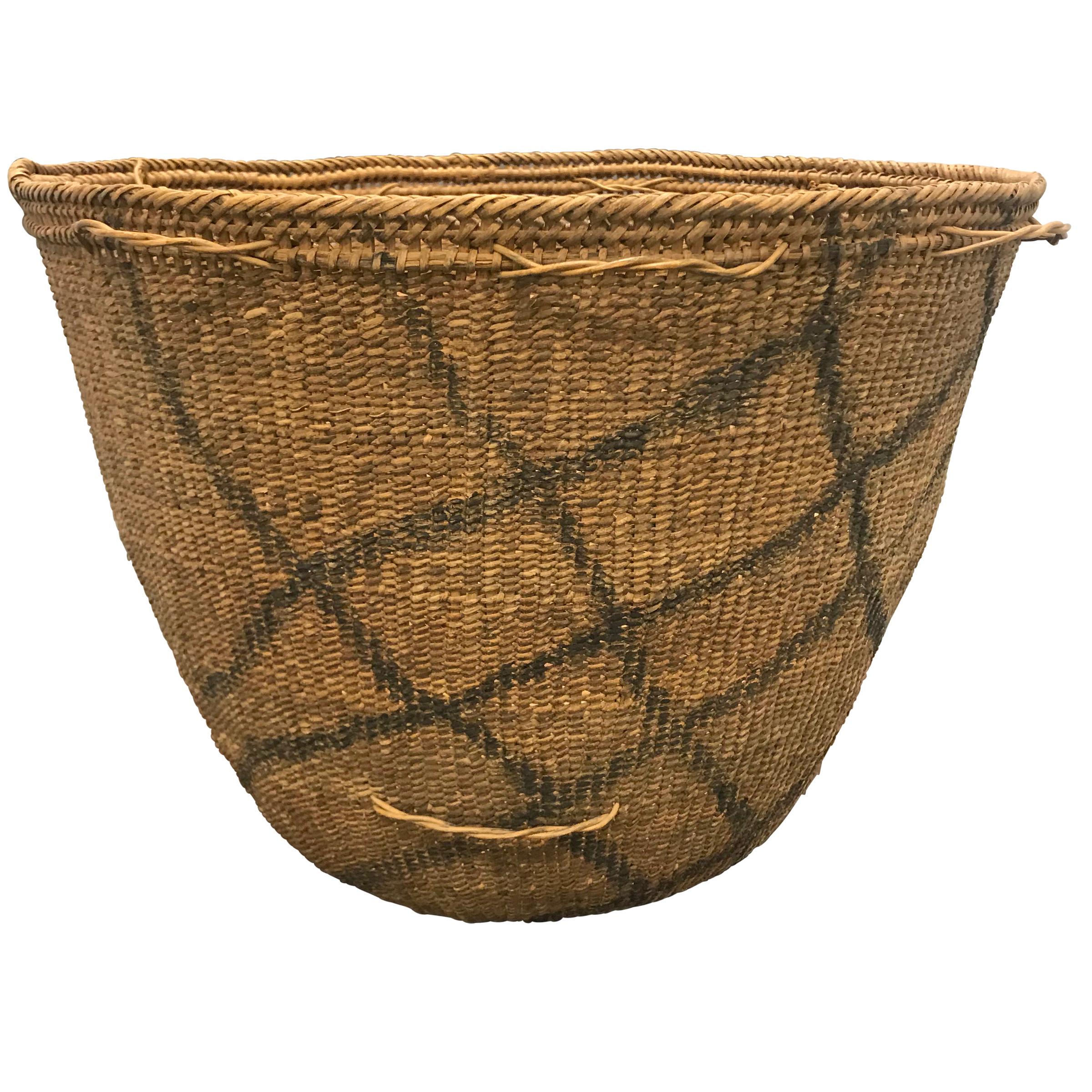 A 20th century Yanomami gathering basket decorated with charcoal line drawings on the exterior. This basket is tightly handwoven of natural fibers with several inner rings for stability, and palm leaf straps. Straps are tied around the small loops