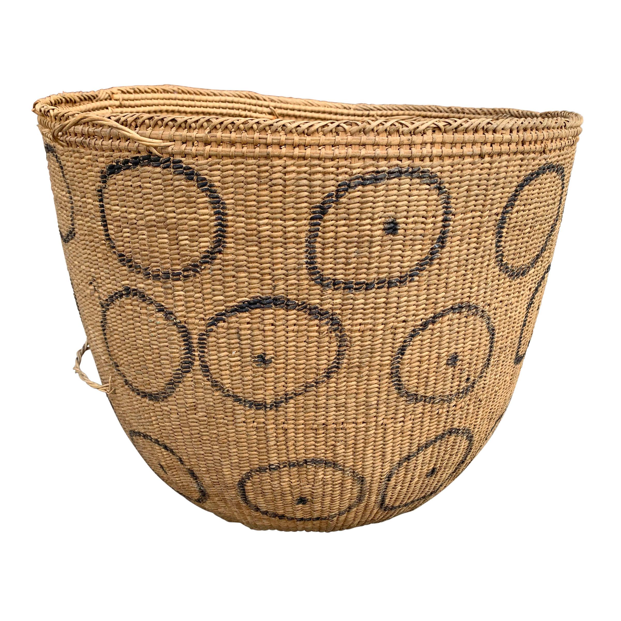 A 20th century Yanomami gathering basket decorated with charcoal drawn circles with dots on the exterior. This basket is tightly handwoven of natural fibers with several inner rings for stability. Straps are usually tied around the small loops