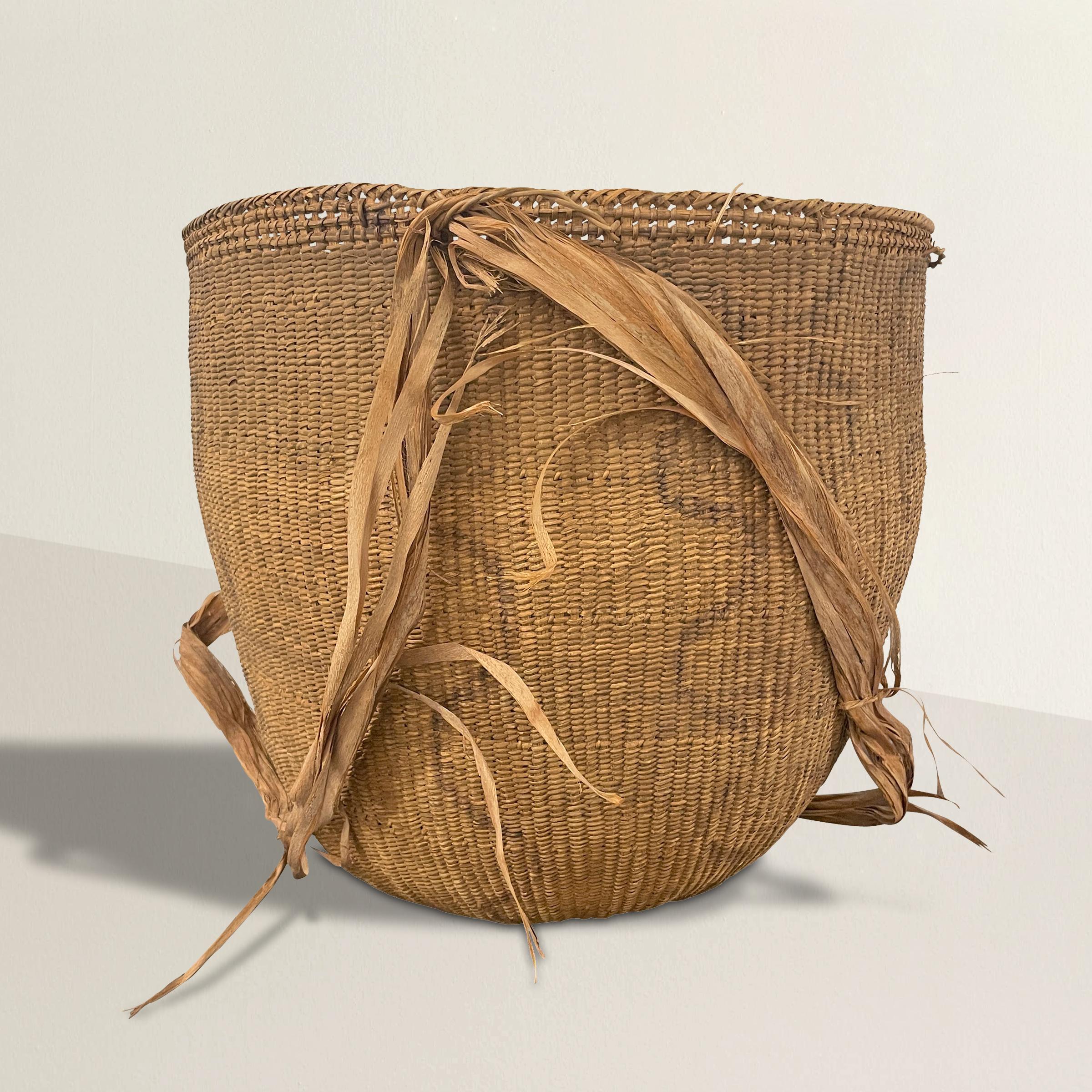 A 20th century Yanomami gathering basket decorated with charcoal line drawings on the exterior. This basket is tightly handwoven of natural fibers with several inner rings for stability, and palm leaf straps. Originally the straps placed over the