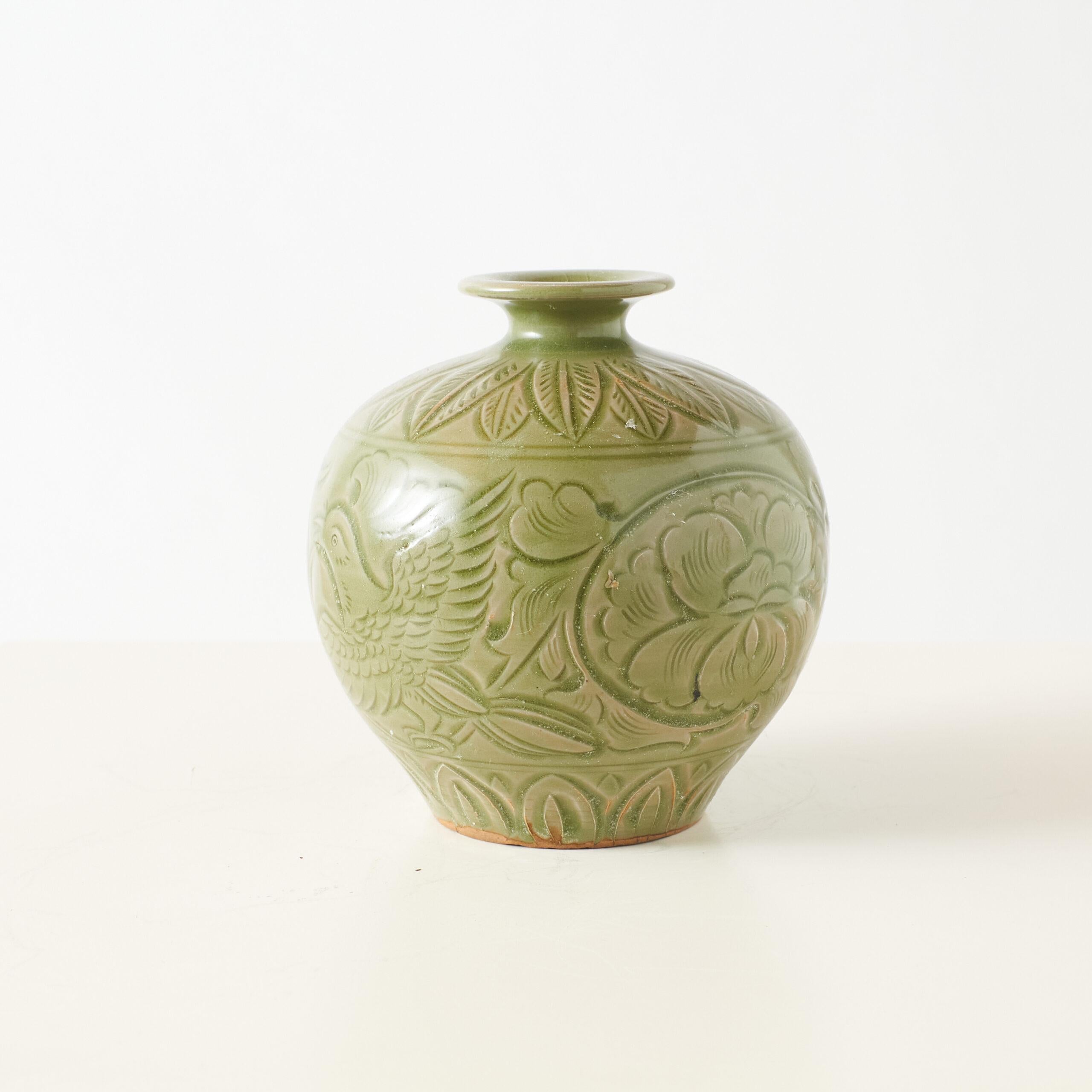 Yaozhou Style Celadon Vase with Carved Peony Motif

A round-bodied vase with a narrow neck and slightly flared lip, finished in a soft green celadon glaze. The surface features carved peony blooms and leaf patterns in symmetrical relief, a hallmark