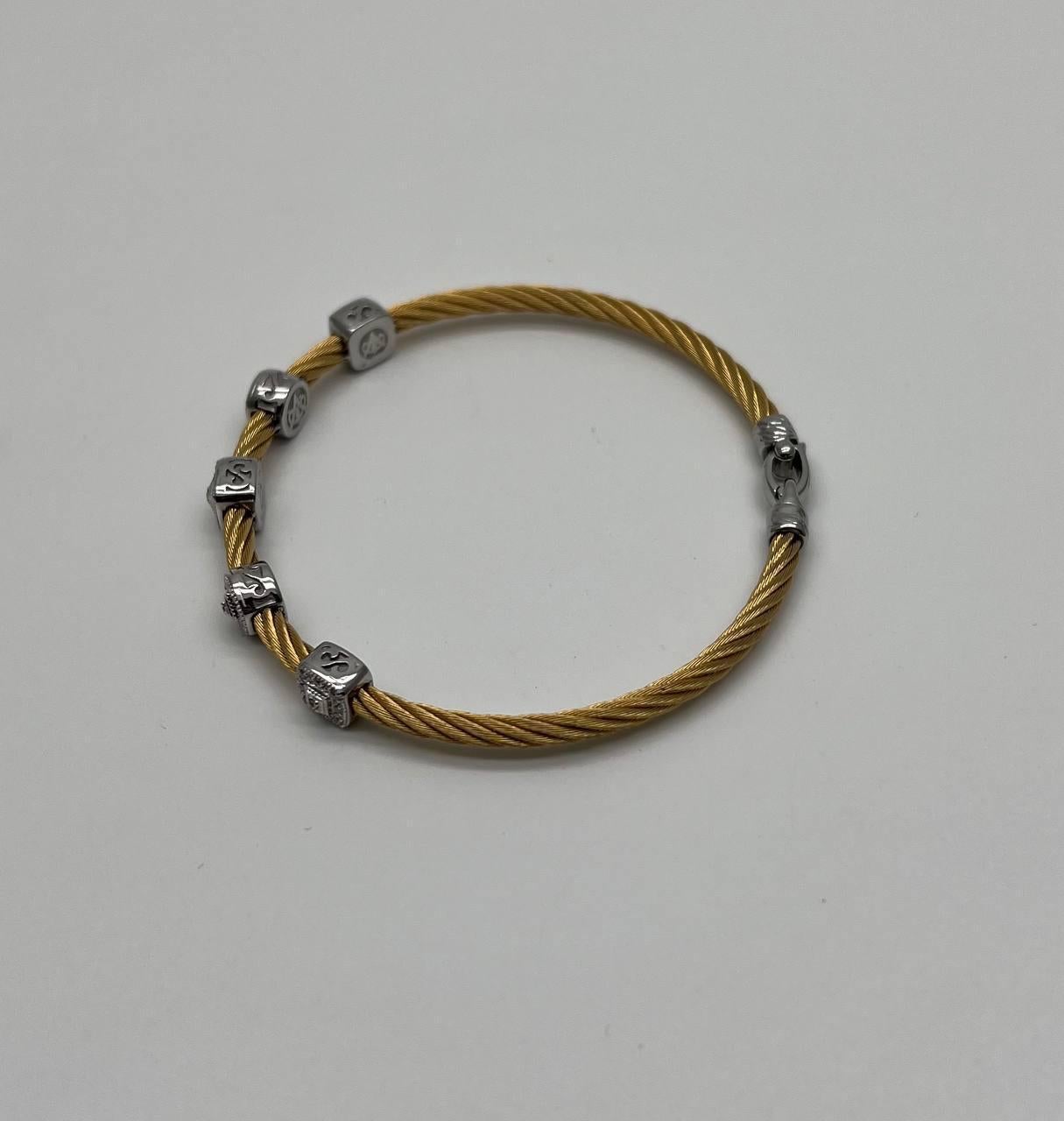 Realizzato con un cavo d'acciaio dorato attorcigliato, questo pezzo presenta cinque accenti quadrati in oro bianco 18 carati equamente distanziati lungo la sua lunghezza. Ogni accento è impreziosito da dettagli intricati che catturano la luce,