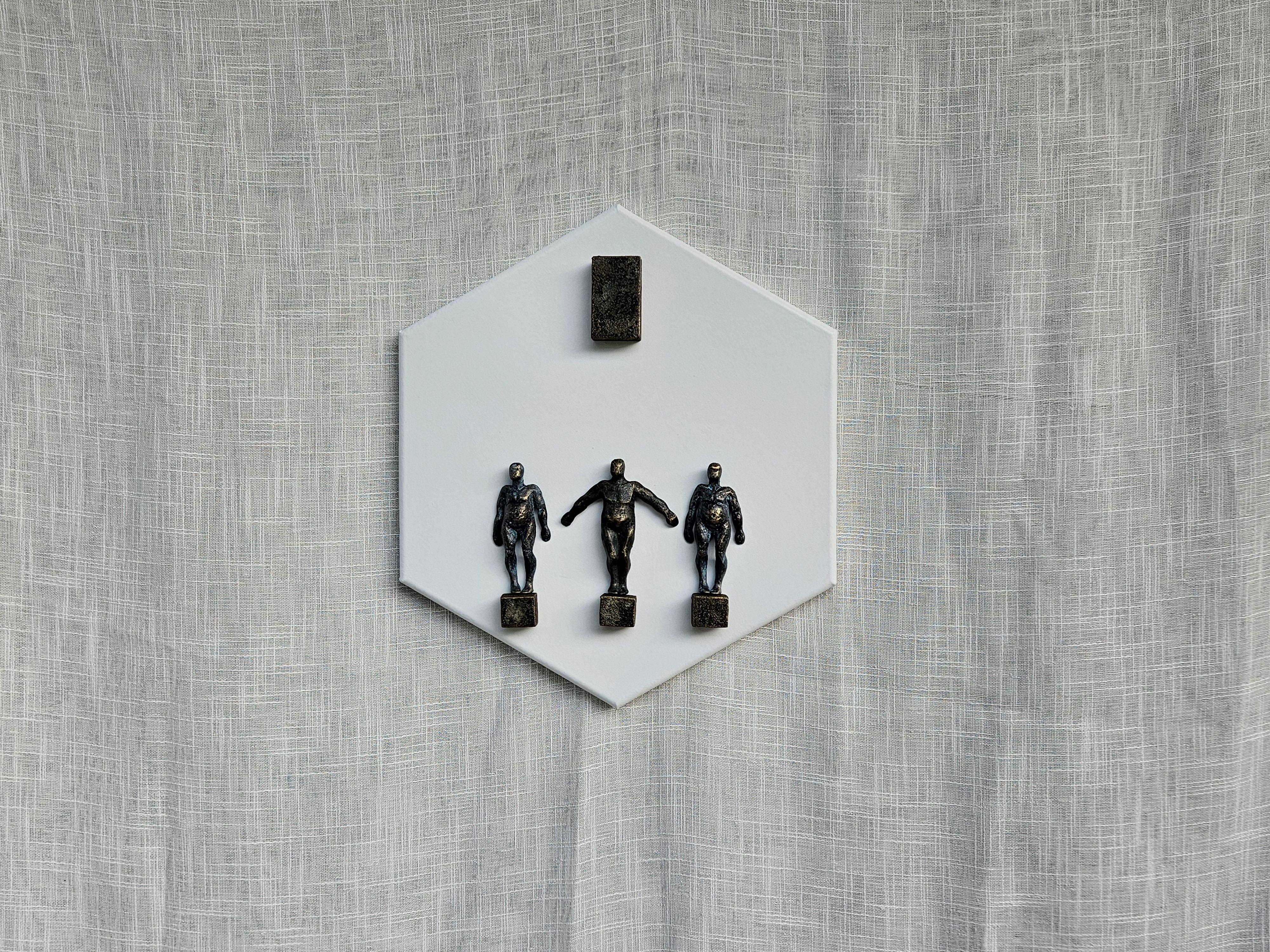 <p>Artist Comments<br>Three human figures stand separately on a square platform, evoking stability and timelessness. A rectangular block hovers above them. The white hexagonal base symbolizes perfection and universal connection, reinforcing the idea