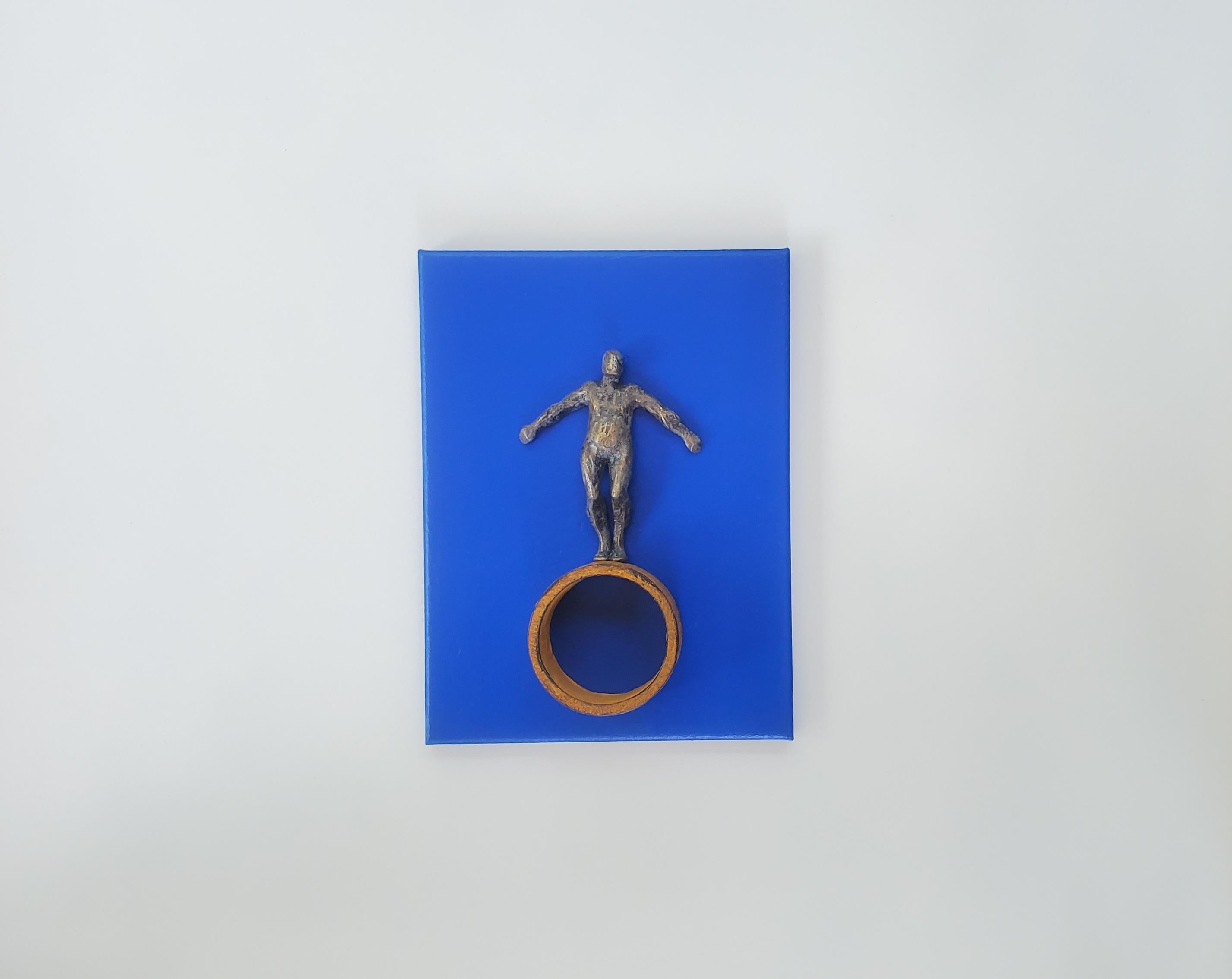 <p>Artist Comments<br>Artist Yelitza Diaz shows a bronze-colored figure balancing itself on a round structure attached to a solid blue background. Inspired by minimalism, she considers the possibility of contradicting the style by including