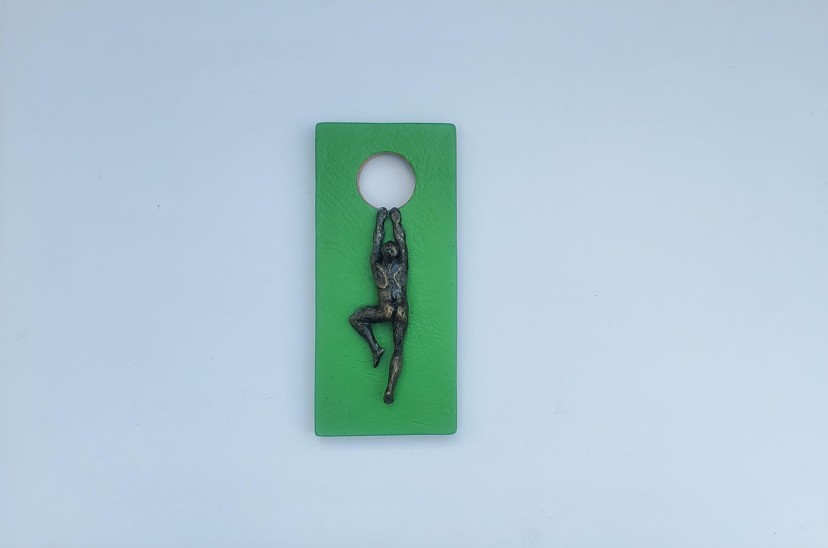 <p>Artist Comments<br>Artist Yelitza Diaz exhibits a man climbing a carved wooden structure painted in green. She creates the nude form with resin and paints its body bronze for a metallic impression. The hole depicts a full moon, representing the