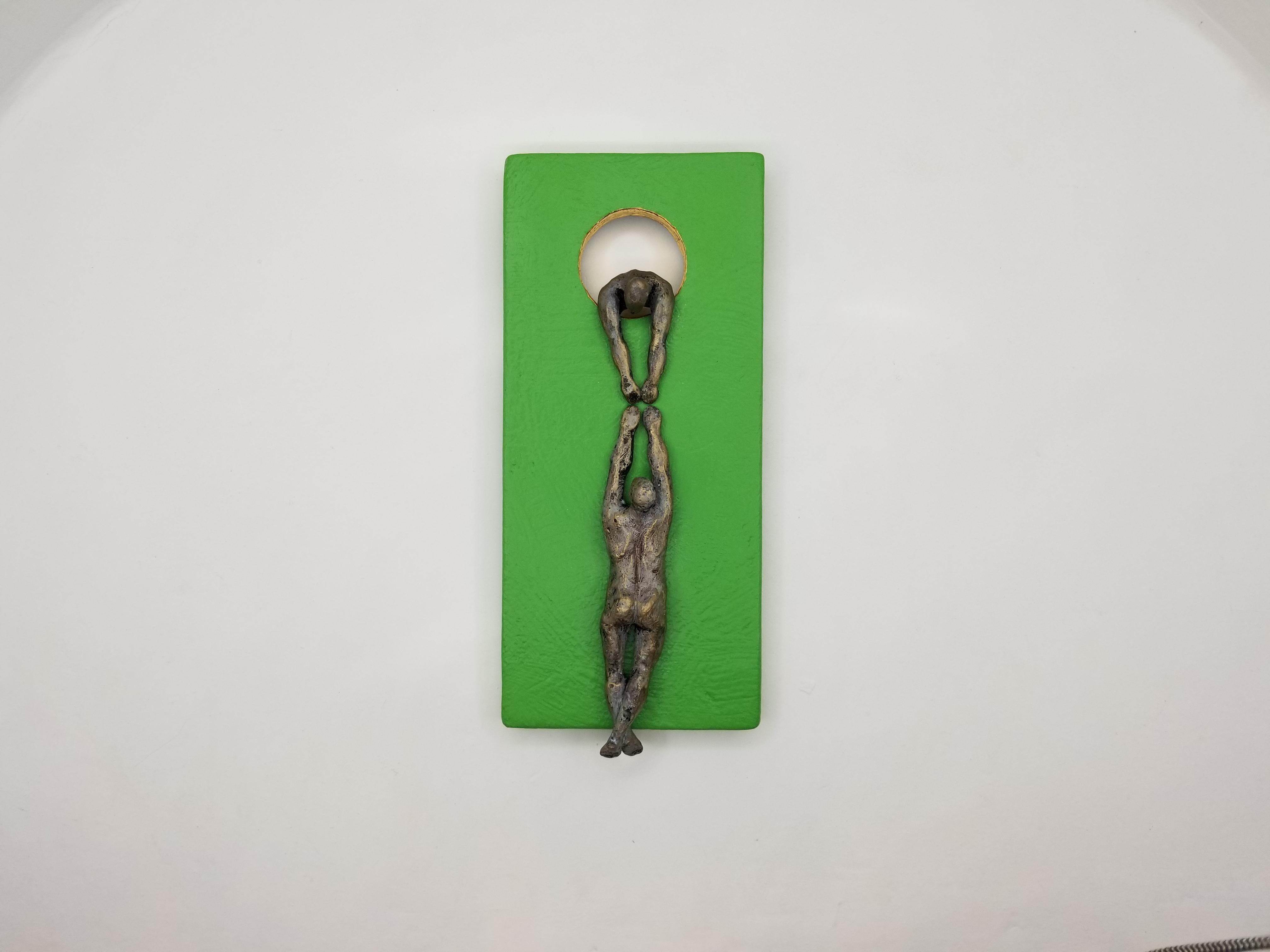 <p>Artist Comments<br>Artist Human Yelitza Diaz demonstrates two figures, one helping the other climb a green wooden structure. She creates the figures with resin and paints their bodies bronze for a metallic impression. The carved hole depicts a