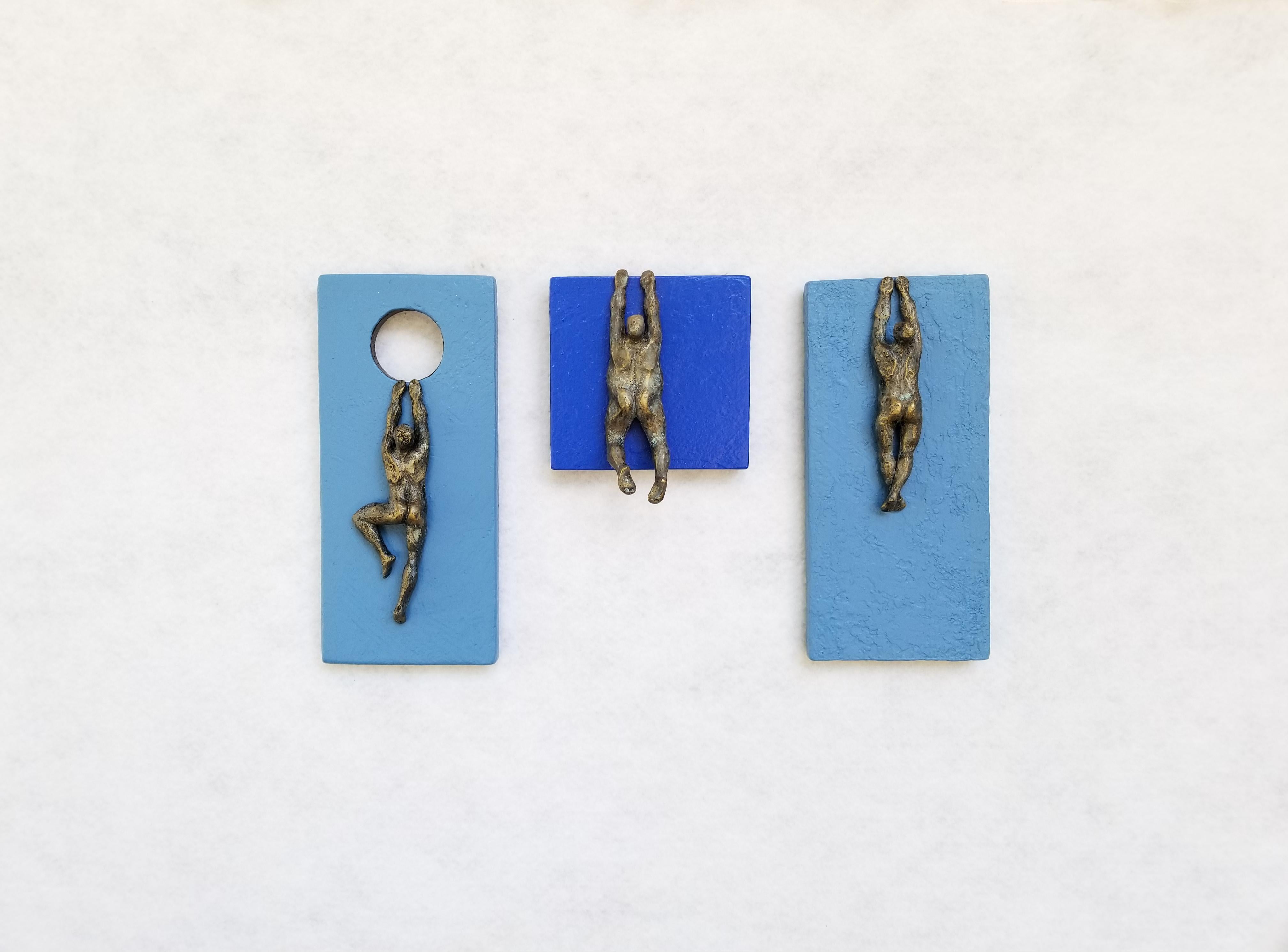<p>Artist Comments<br>Artist Yelitza Diaz displays a modern sculpture of three bronze figures climbing geometric designs. The first figure clings to a circular cavity carved from a pale blue rectangular panel. The remaining two figures hang by the
