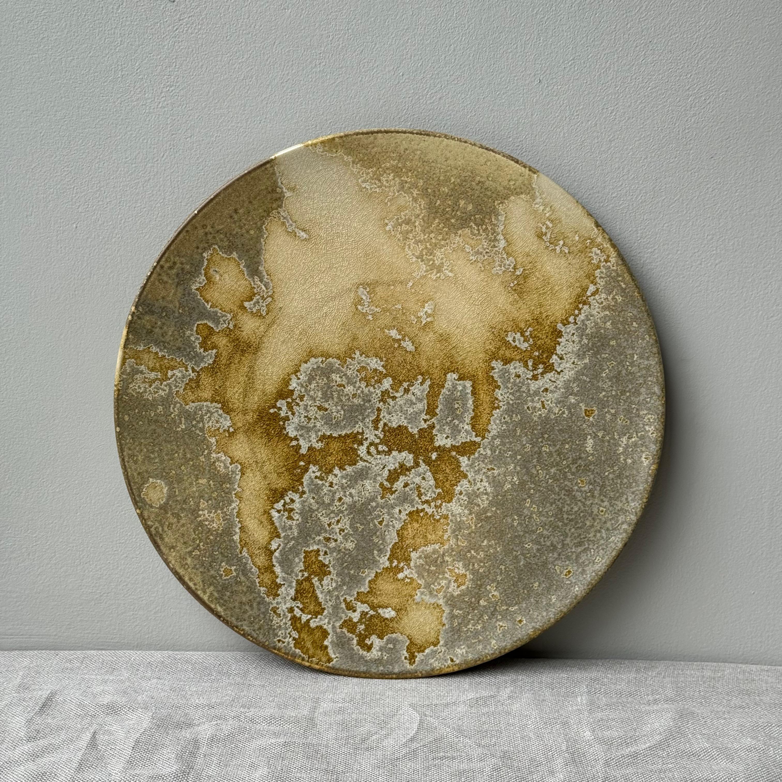 A flat stoneware charger made and designed in Denmark by K H Würtz.A flat stoneware charger with tones of yellow, gold and green colours. The lighter, shinier portions of this glaze coalesce to create an almost atlas-like effect across the flat