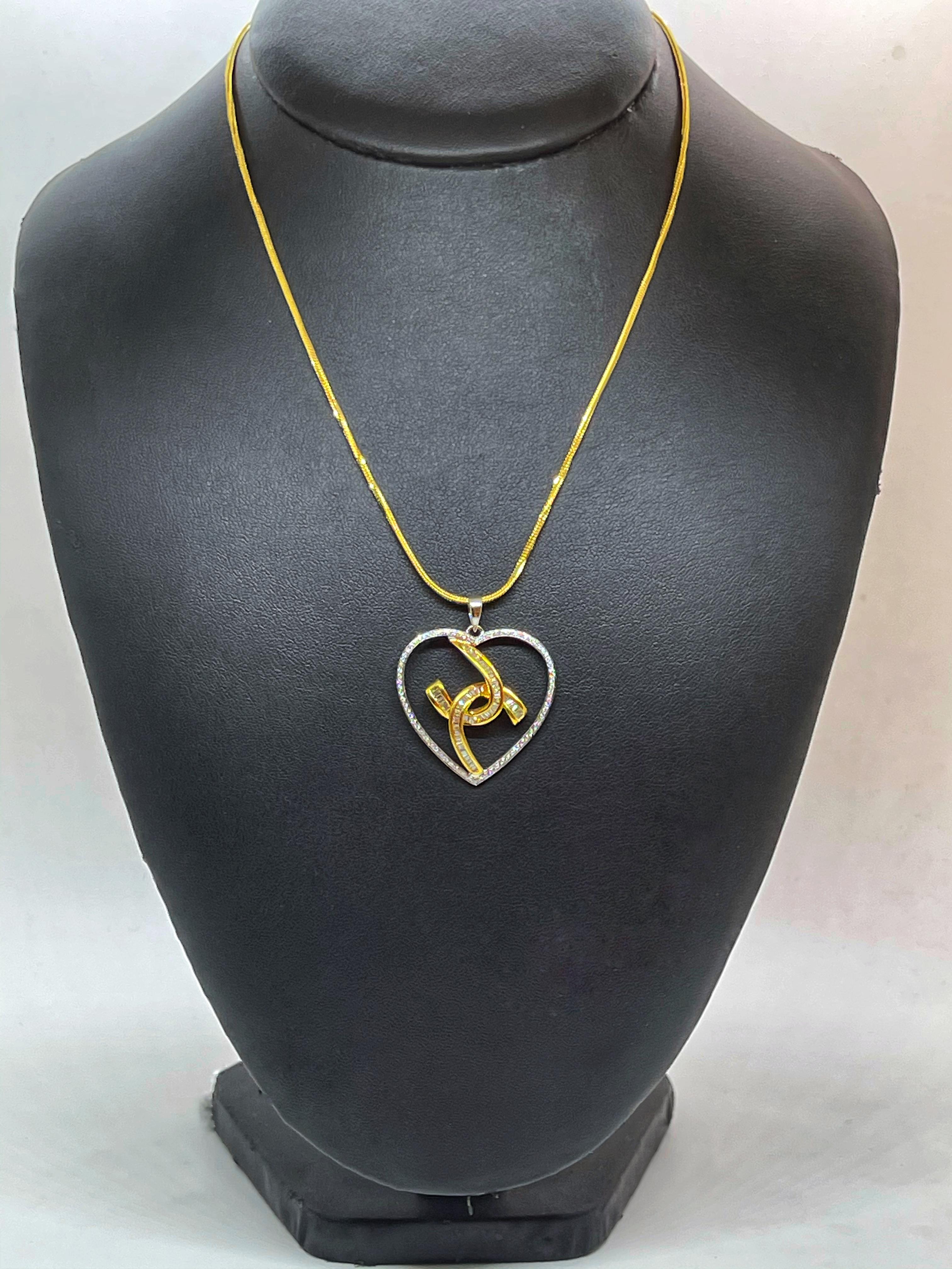 Elegant heart shaped yellow and white 18K diamond necklace. Two curved crossed lines in the center are paved with buguette cut diamonds. the heart in white gold is paved with round brilliant cut diamonds. The pendant goes together with a 18K yellow