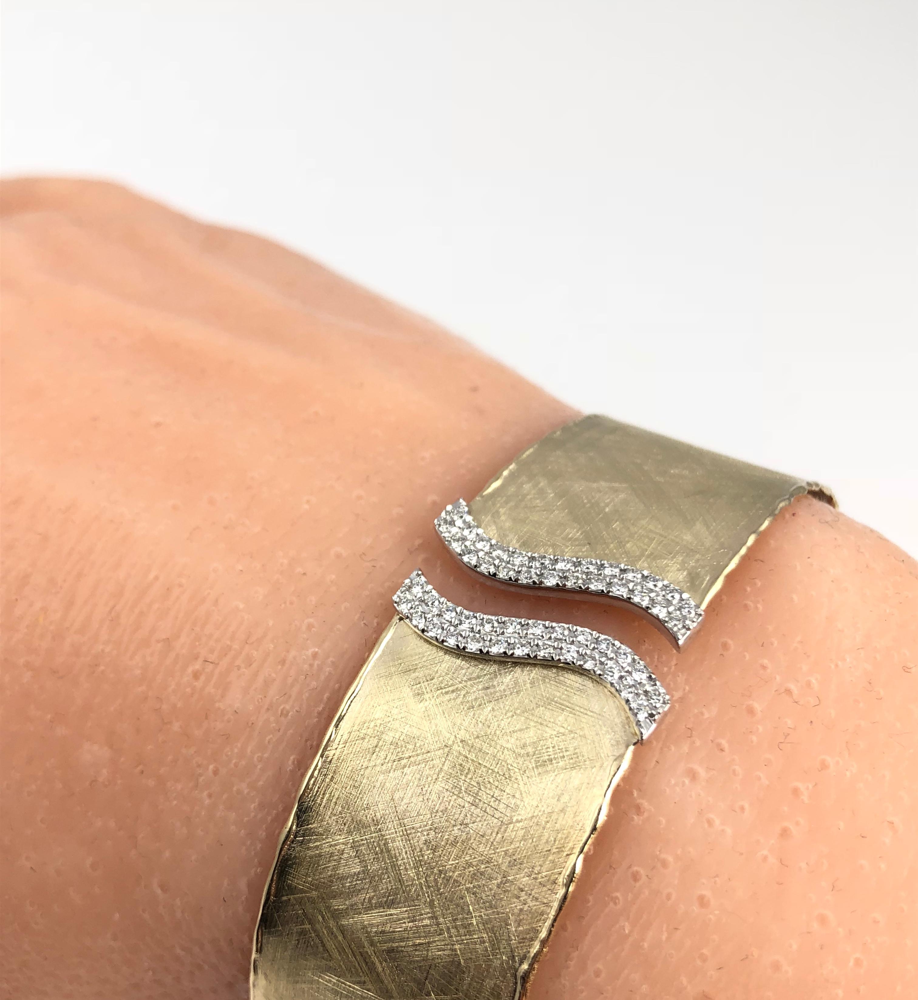 (DiamondTown) This rustic bangle has a brushed yellow gold design, accented by two swirls of round white diamonds at the opening. The bangle is flexible enough to pass over the hand, without any hinge or buckle.

The bangle is set in 14k Yellow and
