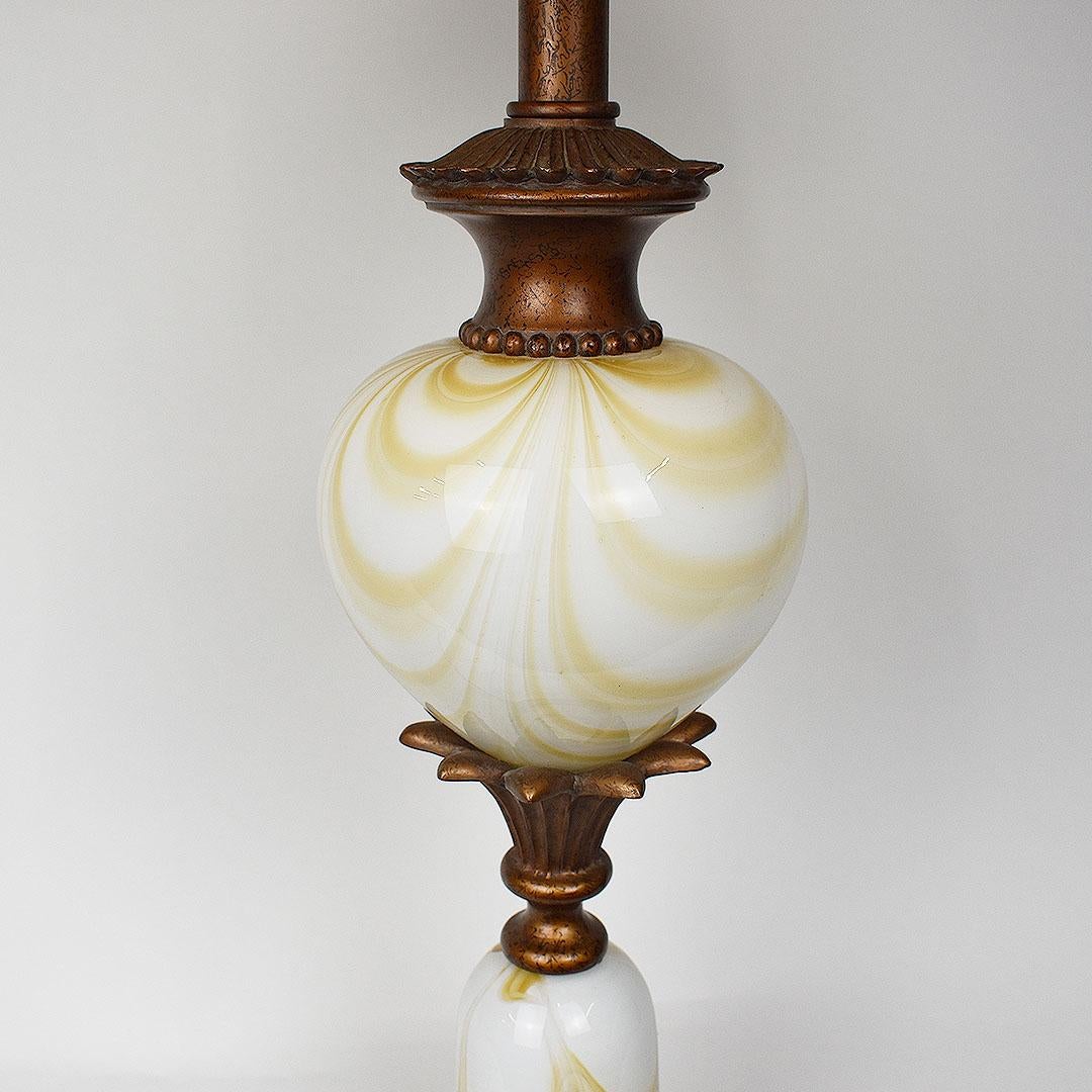 Lampe en verre d'art de style Murano avec des boules en verre d'art jaunes et blanches empilées. Les boules de verre sur le corps de la lampe sont séparées par des détails en métal faux bois. 

Il repose sur une base métallique à quatre pieds.