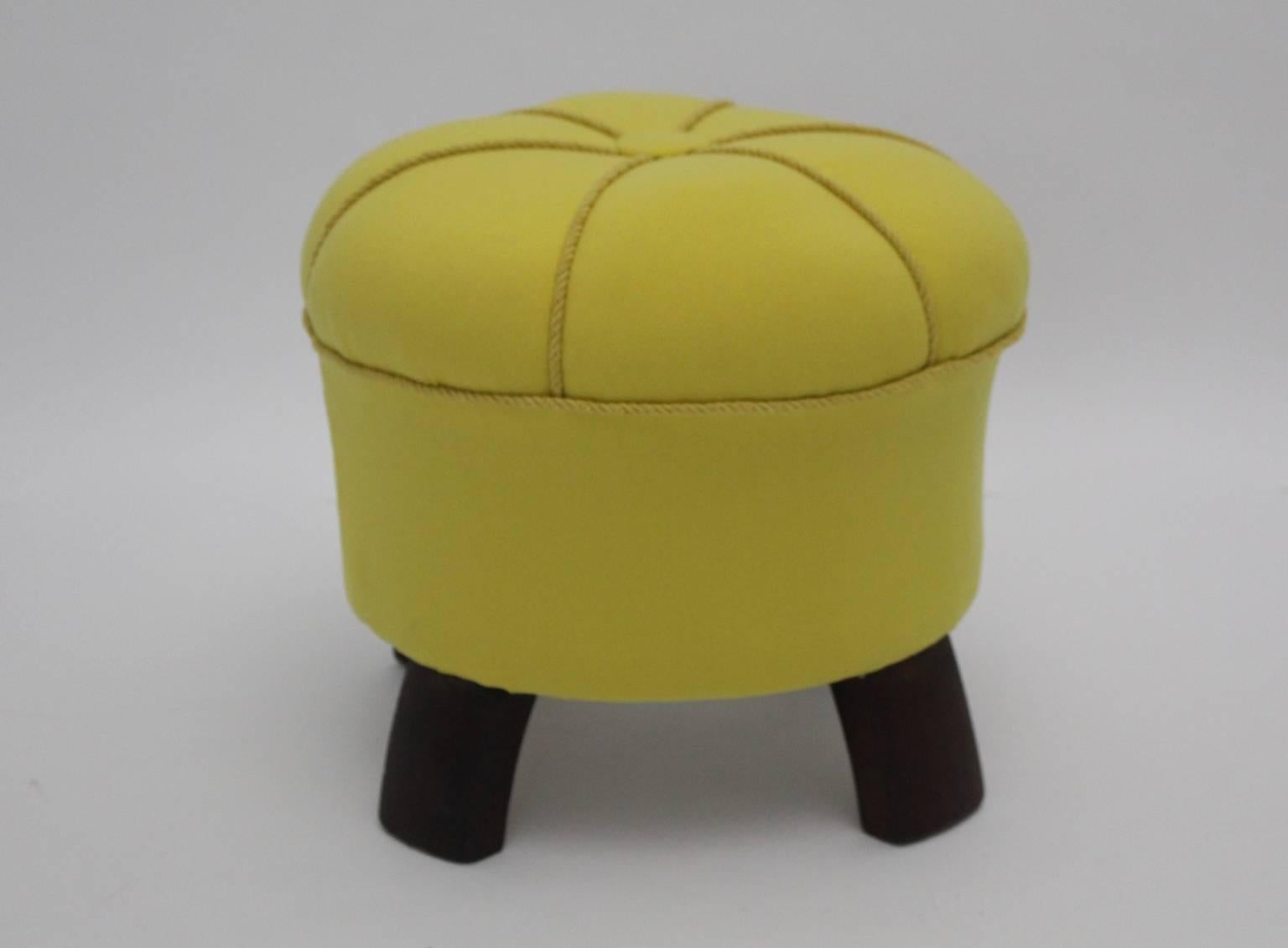 A yellow art deco vintage pouf, which was designed and manufactured in Austria, 1930s.
The renewed covering of the footstool is made of lemon yellow textile fabric and yellow cords.

The beechwood feet are carefully cleaned and brown stained.
The