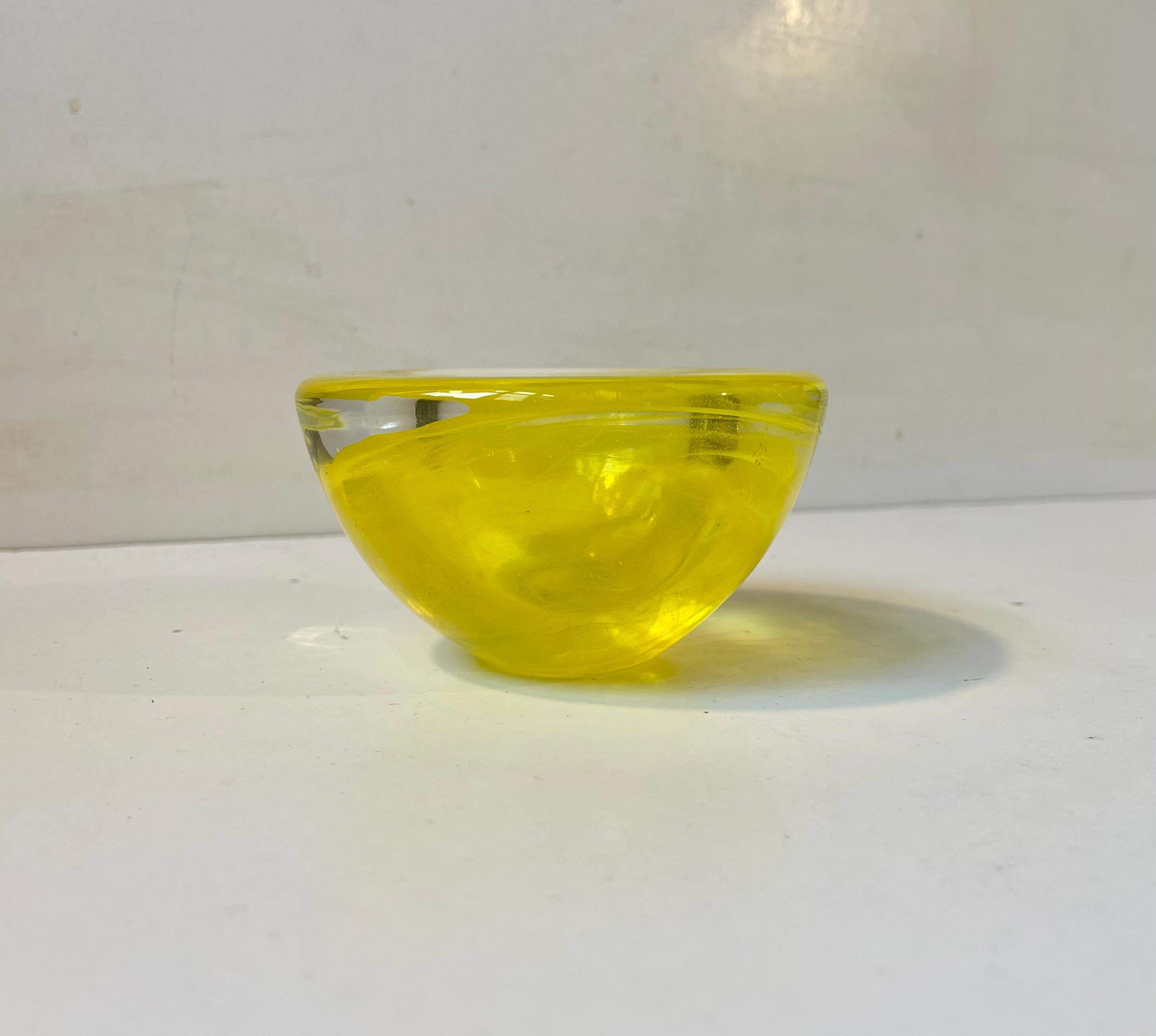 Cuenco pequeño de vidrio artístico, grueso, pesado y de color limón, procedente de Kosta Boda (Suecia). Fue diseñado por Anna Ehrner a mediados de la década de 1980. El cuenco se llama Atolón y presenta remolinos en amarillo y transparente en el